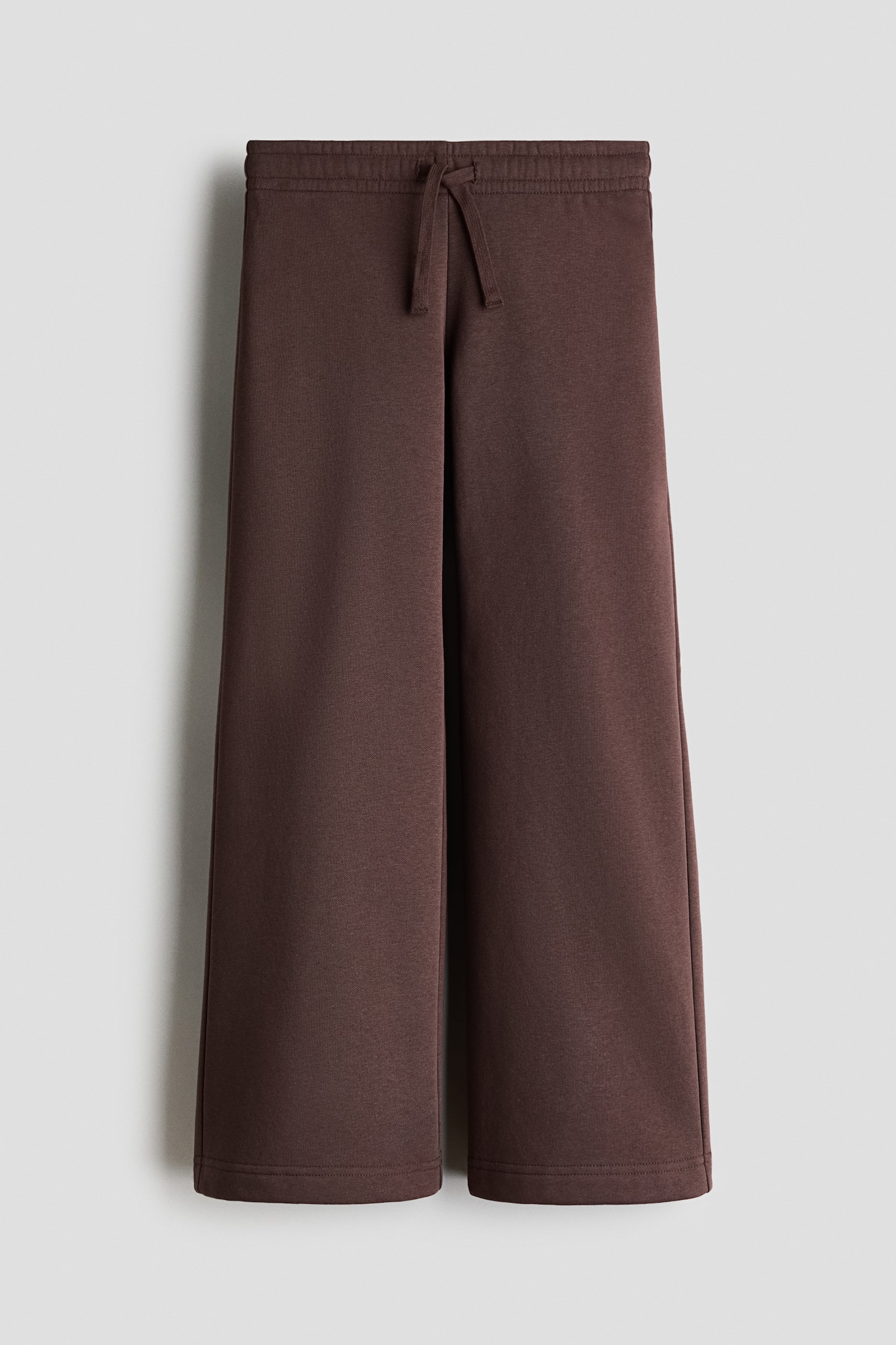 Dark brown track pants are shown from the front, featuring a straight-leg silhouette and an elasticated waistband with a matching drawstring tied at the centre. The pants are made of soft fleece fabric with clean, stitched hems.