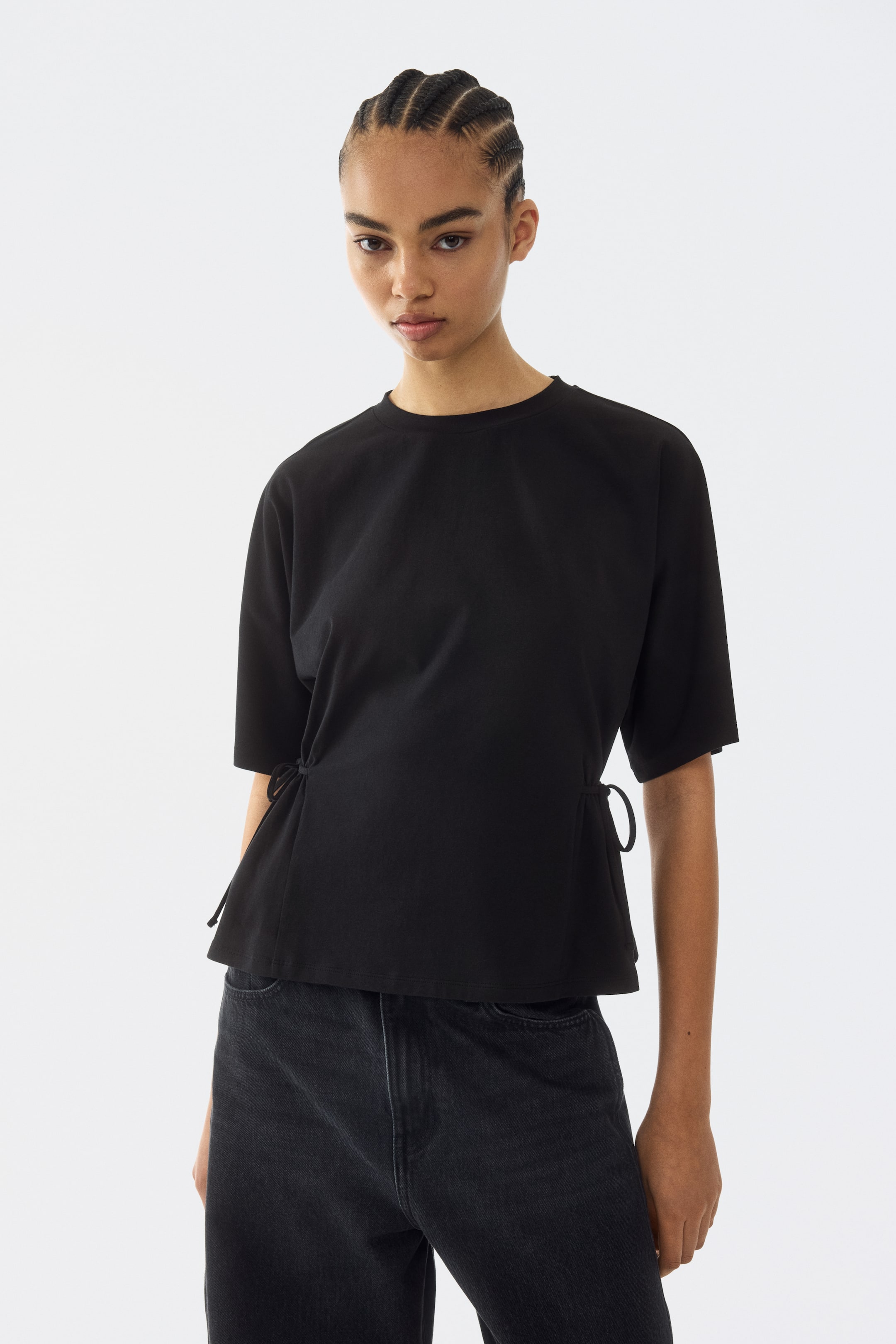 View larger image: The black top comes with a crew neck and short sleeves, featuring adjustable side ties on both sides that create a gathered detail at the hem.