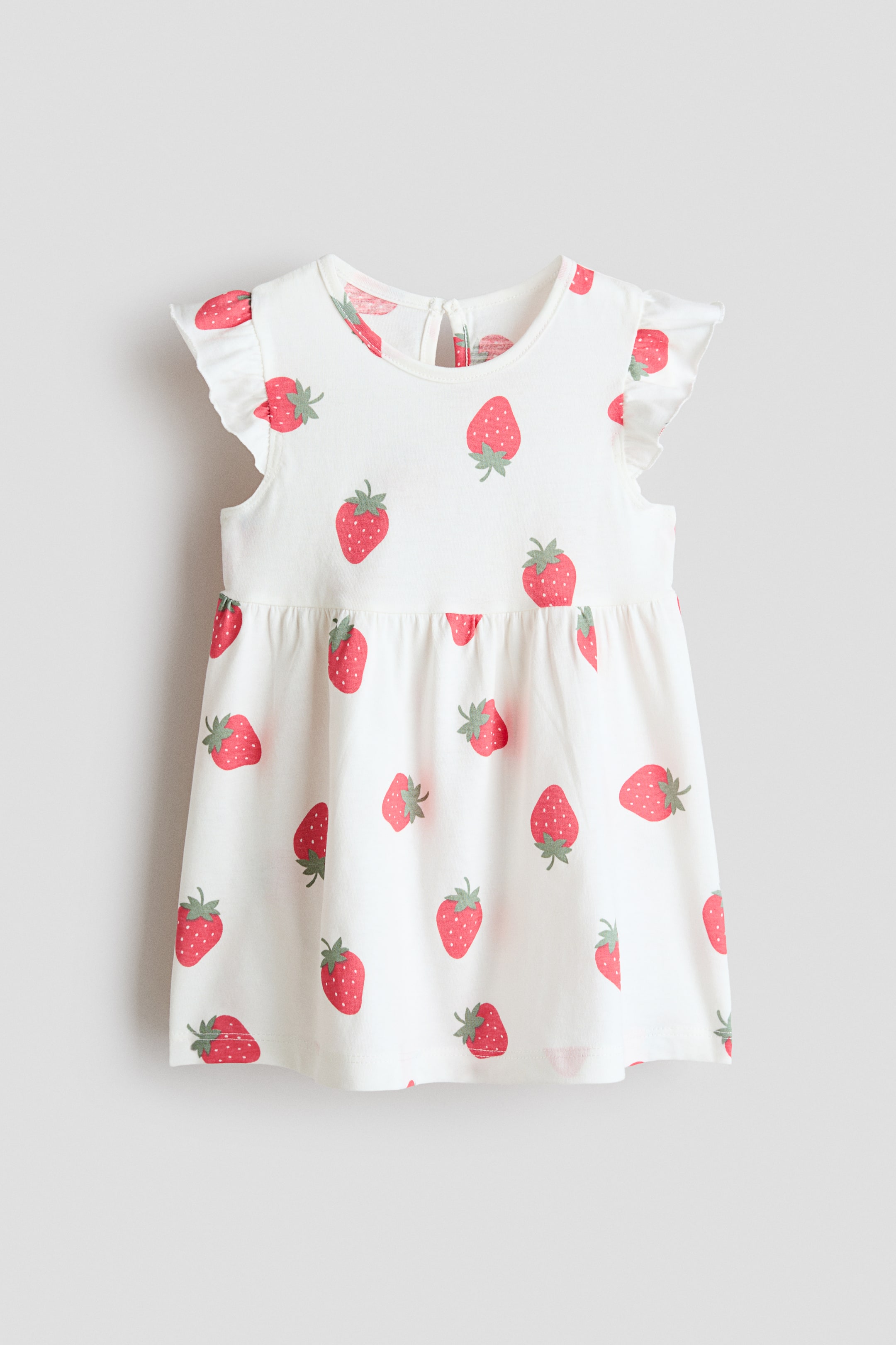 View larger image: A soft, white printed cotton jersey frock is displayed from the front, showcasing a red strawberry motif. It boasts a round neckline, flutter sleeves, a keyhole opening with a button at the back, gathers at the waist, and a flared skirt.