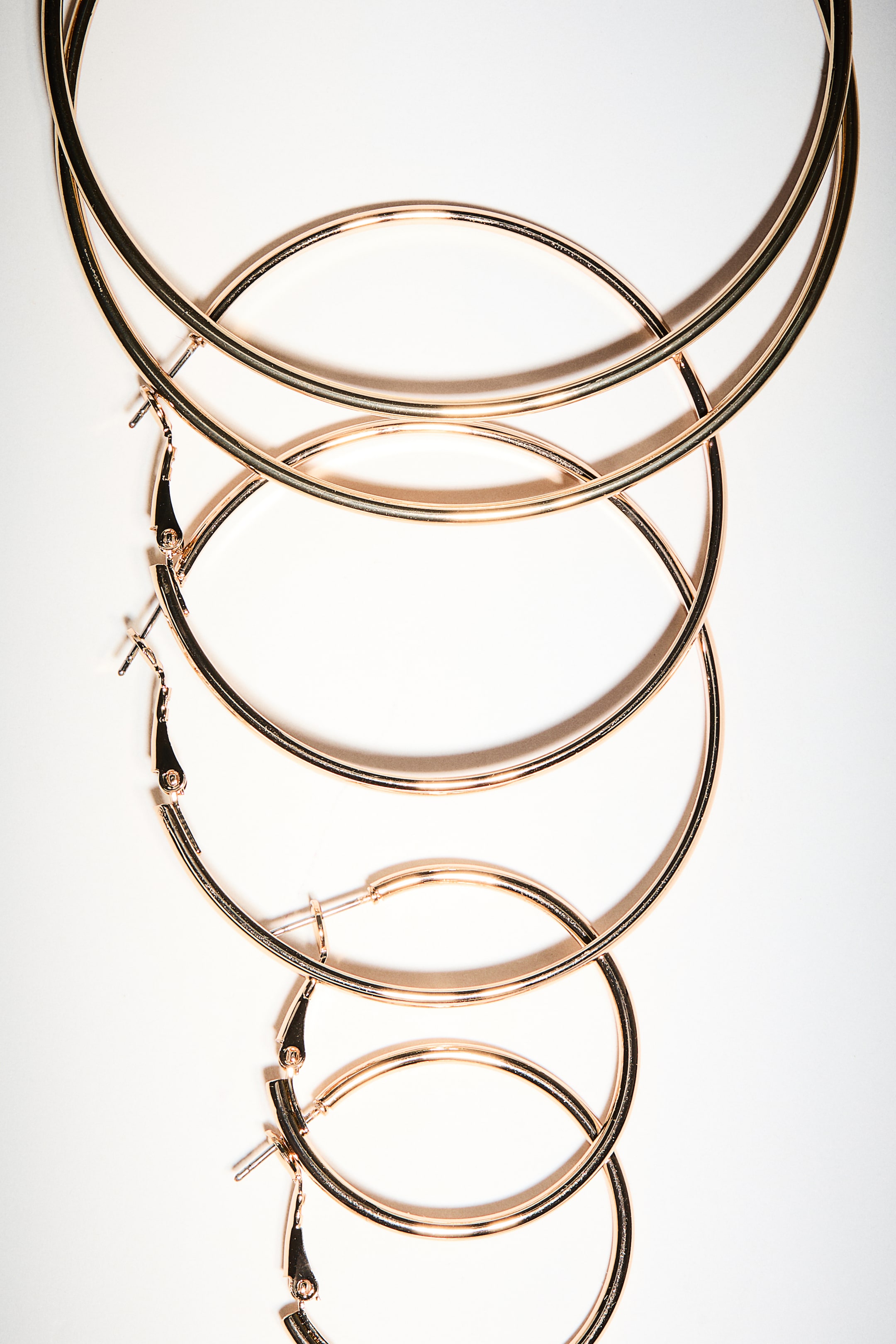 View larger image: Gold-toned hoop earrings are lying flat and overlapping, arranged vertically from largest at the top to smallest at the bottom. The earrings are showcasing their circular shape and visible post closures.