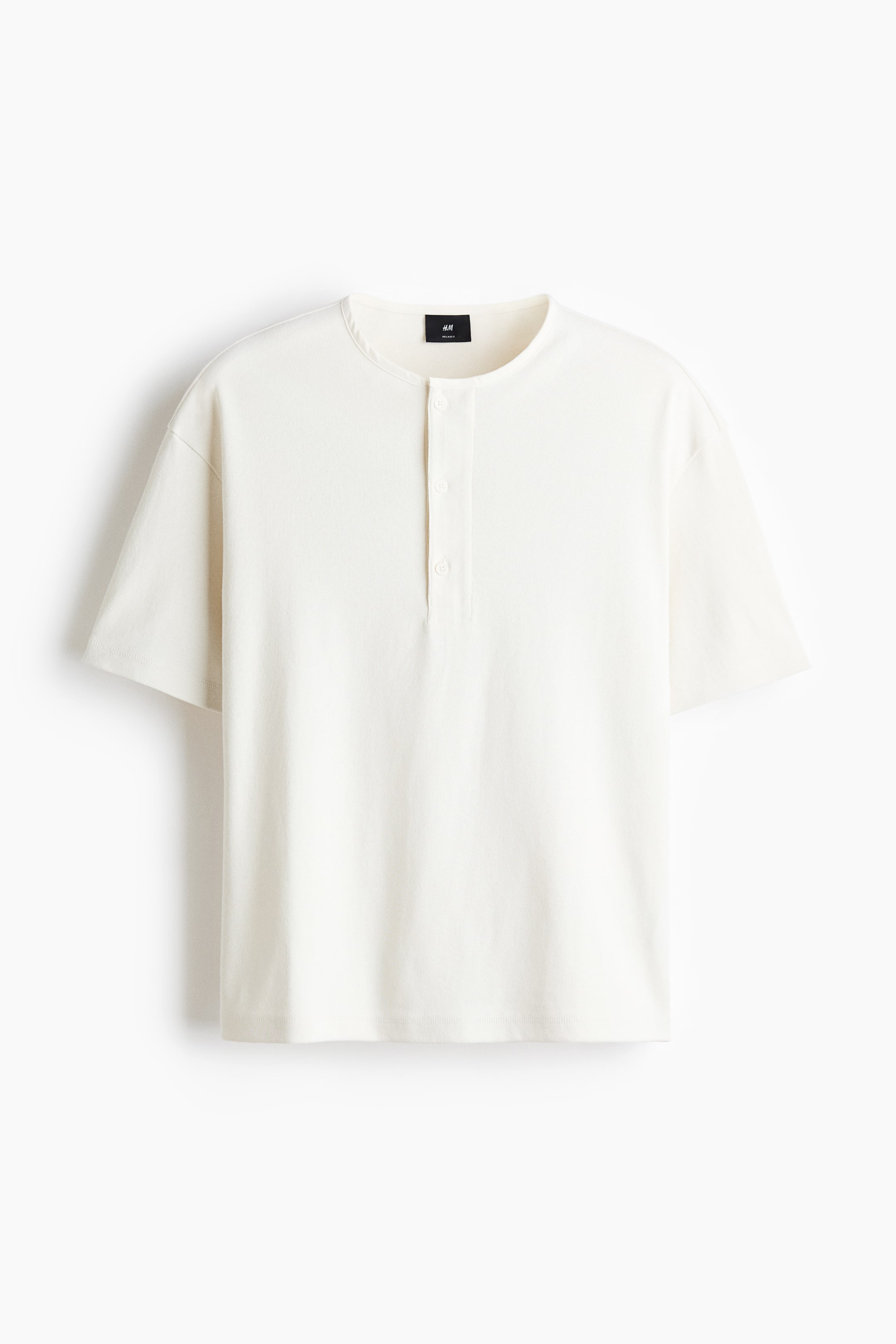 Größeres Bild ansehen: Ein cremefarbenes Henley-Shirt mit kragenlosem Ausschnitt, einer Knopfleiste mit drei Knöpfen und kurzen Ärmeln. Ein schwarzes Markenetikett ist auf dem inneren Rückenausschnitt sichtbar.