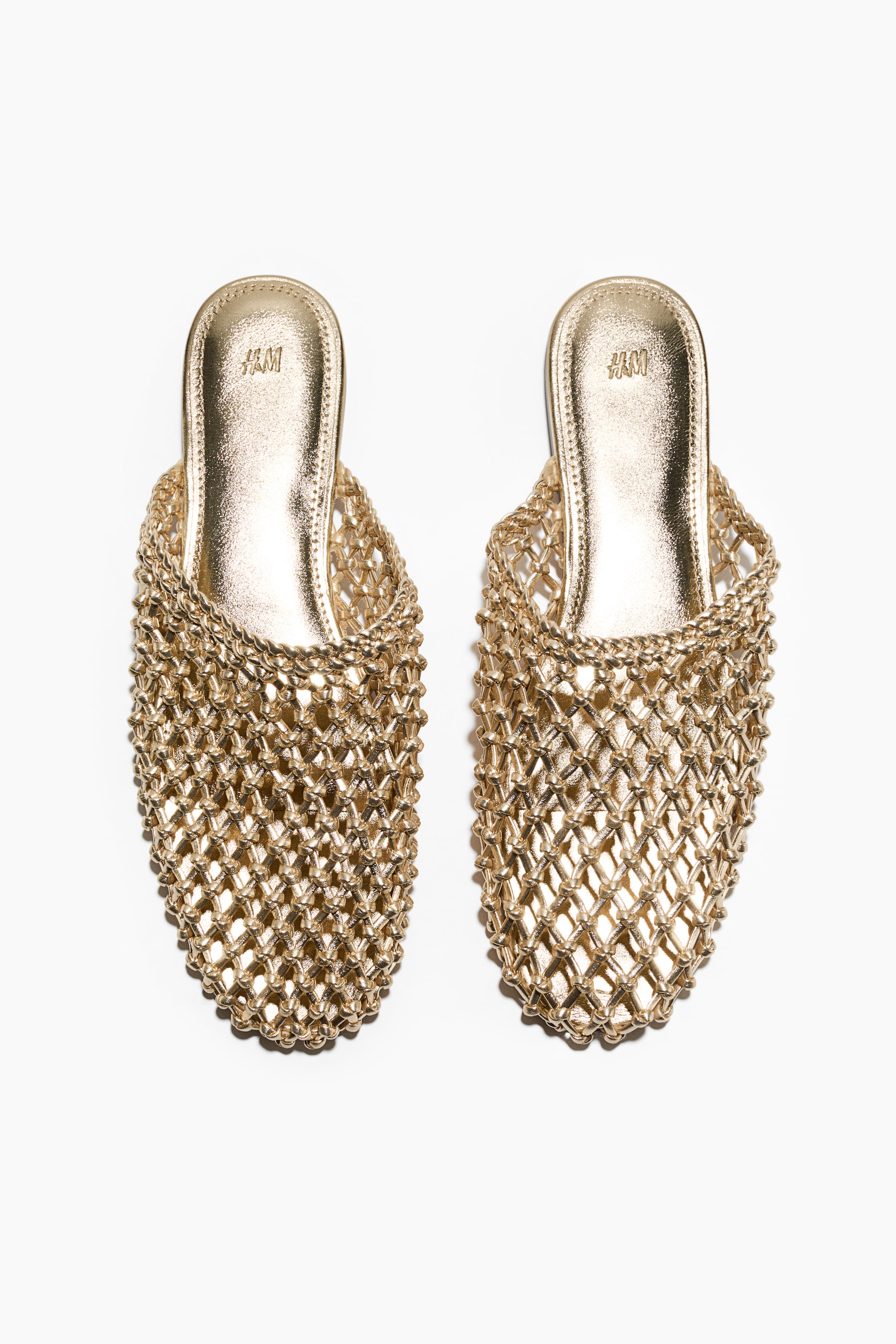 Ver imagem maior: Um par de mules metálicos dourados apresenta uma parte superior em forma de rede entrelaçada com uma ponta afiada. As palmilhas metálicas douradas visíveis estão gravadas com "H&M" próximo ao calcanhar.