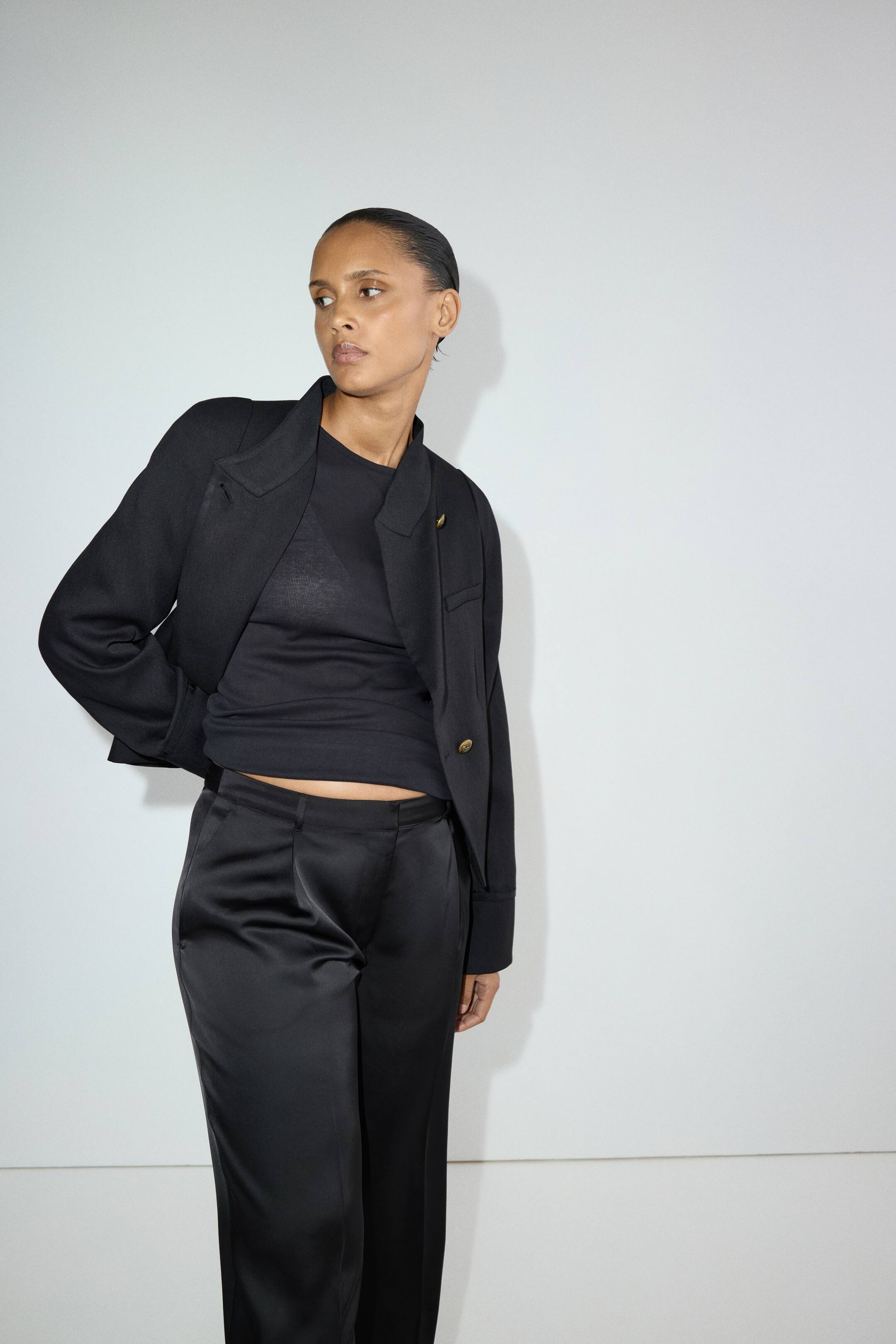 Ampliar la imagen: La modelo lleva puesta una camiseta ajustada negra con cuello redondo y dobladillo de corte recto. La camiseta se usa debajo de una chaqueta negra y se combina con pantalones negros de satén a juego.