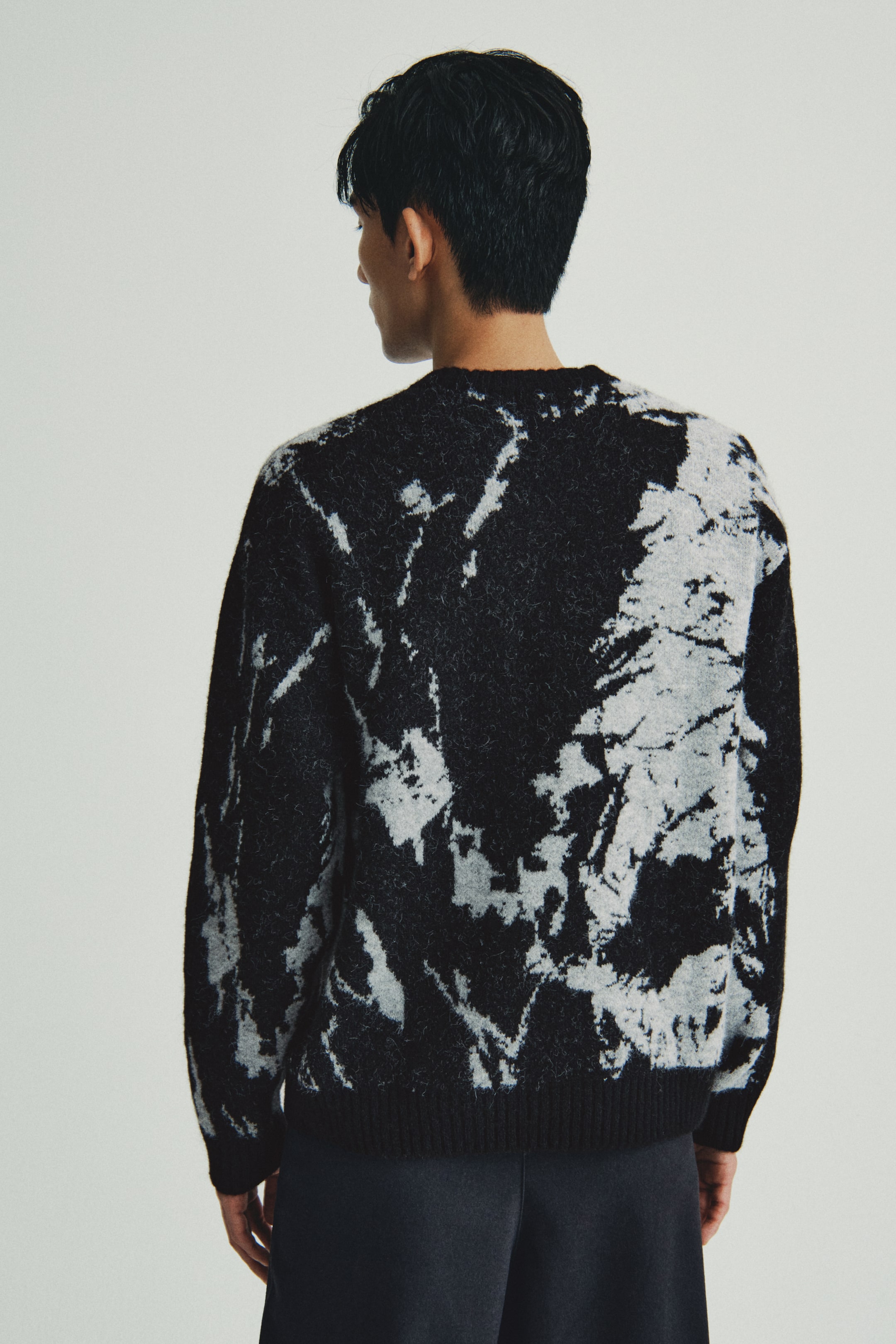 이미지 확대 보기: 스웨터는 뒤에서 보면 검정색과 연한 회색의 추상 패턴이 나타납니다. 그것은 퍼지 니트 질감과 리브드 커프 및 리브드 밑단을 특징으로 하고 있습니다.