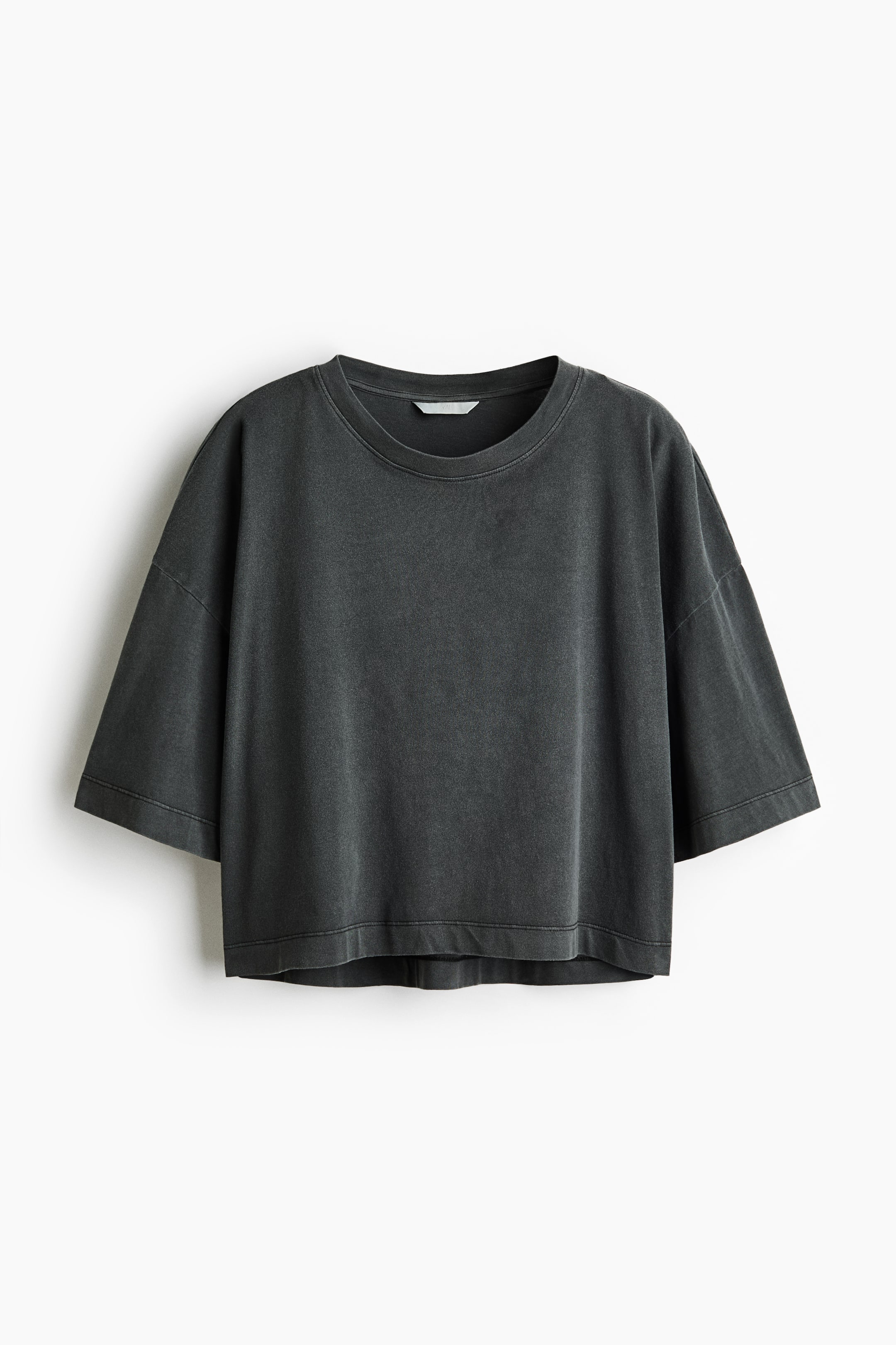 View larger image: A dark grey cropped t-shirt is shown from the front, featuring a crew neck and wide, short sleeves with dropped shoulders. It exhibits a faded, washed appearance and a straight hem with a finished band.