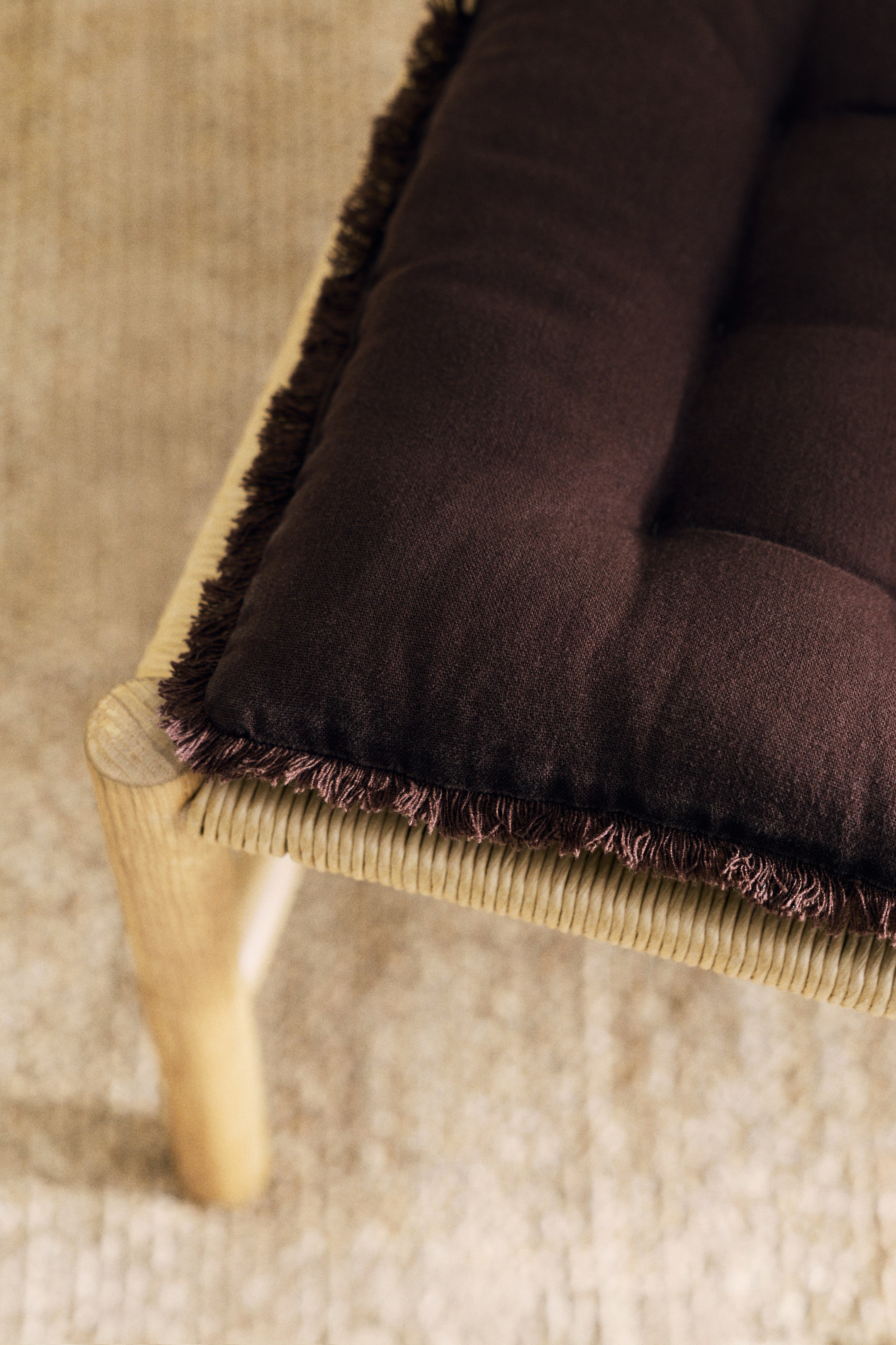 View larger image: A pair of padded seat cushions features a dark brown linen and cotton weave. One cushion displays quilt knots and frayed edges along its perimeter.
