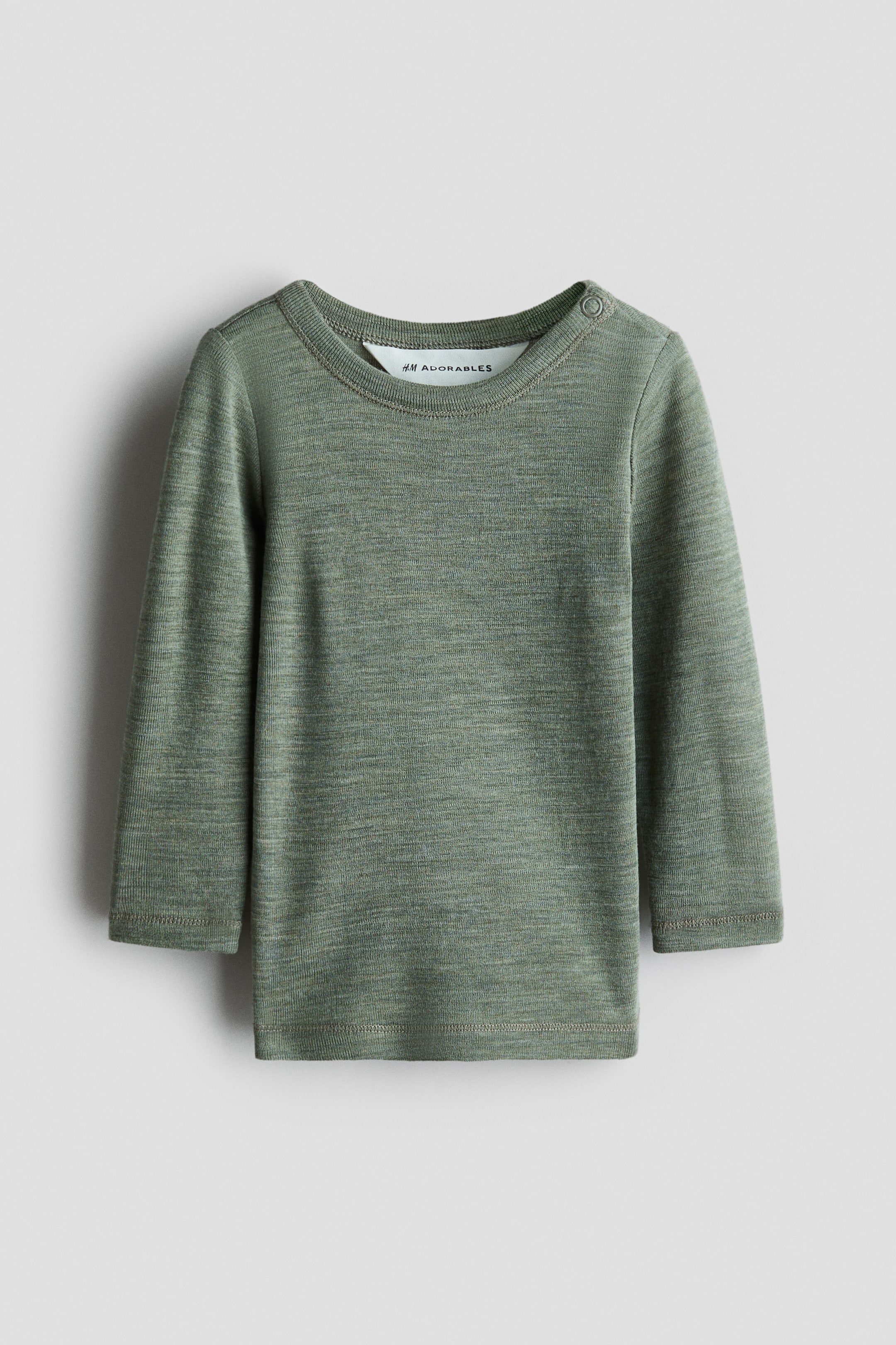 View larger image: Merino wool jersey top. The front of this heathered green long-sleeved top features a crew neck, a single snap button closure on the left shoulder, and a white label with "H&M ADORABLES" visible inside the back neckline.