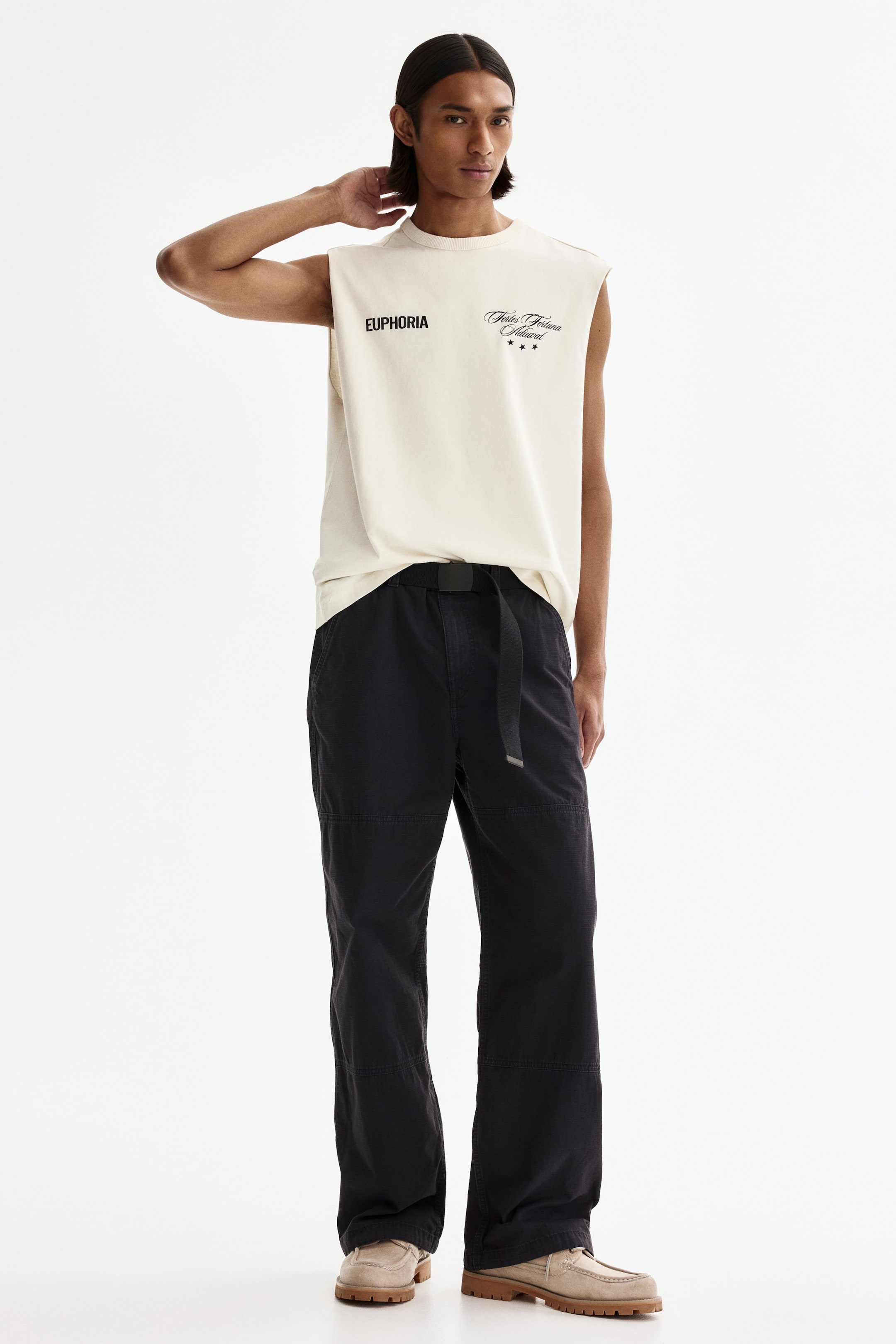 View larger image: An off-white sleeveless T-shirt features the text "EUPHORIA" and a script logo with three stars on the chest. Dark relaxed-fit pants are styled with a black web belt, and light brown moc-toe shoes complete the ensemble, featuring chunky lug soles.