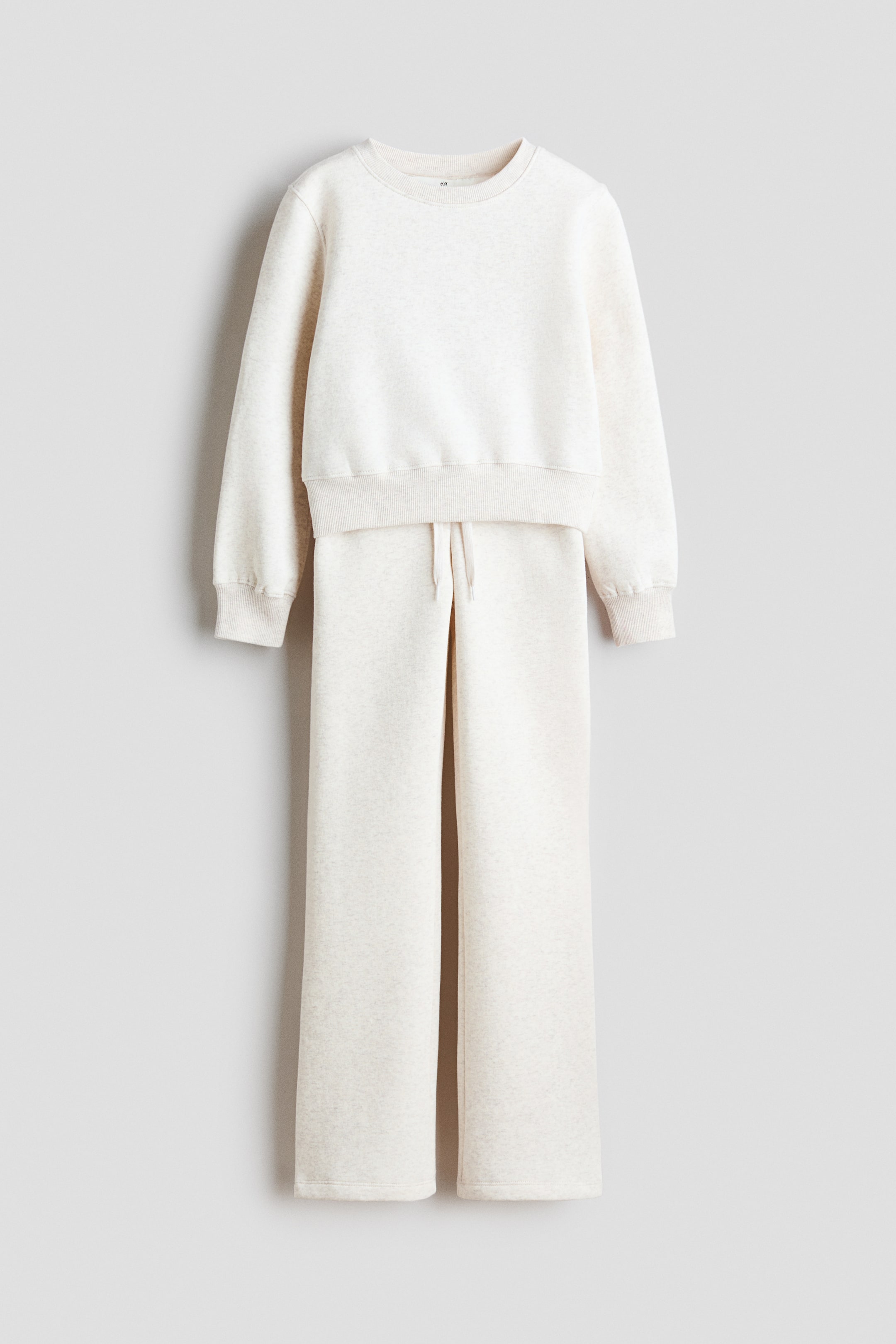 Visualizza immagine più grande: Un set da loungewear a due pezzi in beige chiaro mélange è appeso, presentato frontalmente. La felpa girocollo mostra polsini e orlo a coste, mentre i pantaloni a gamba larga presentano un cordoncino visibile in vita.