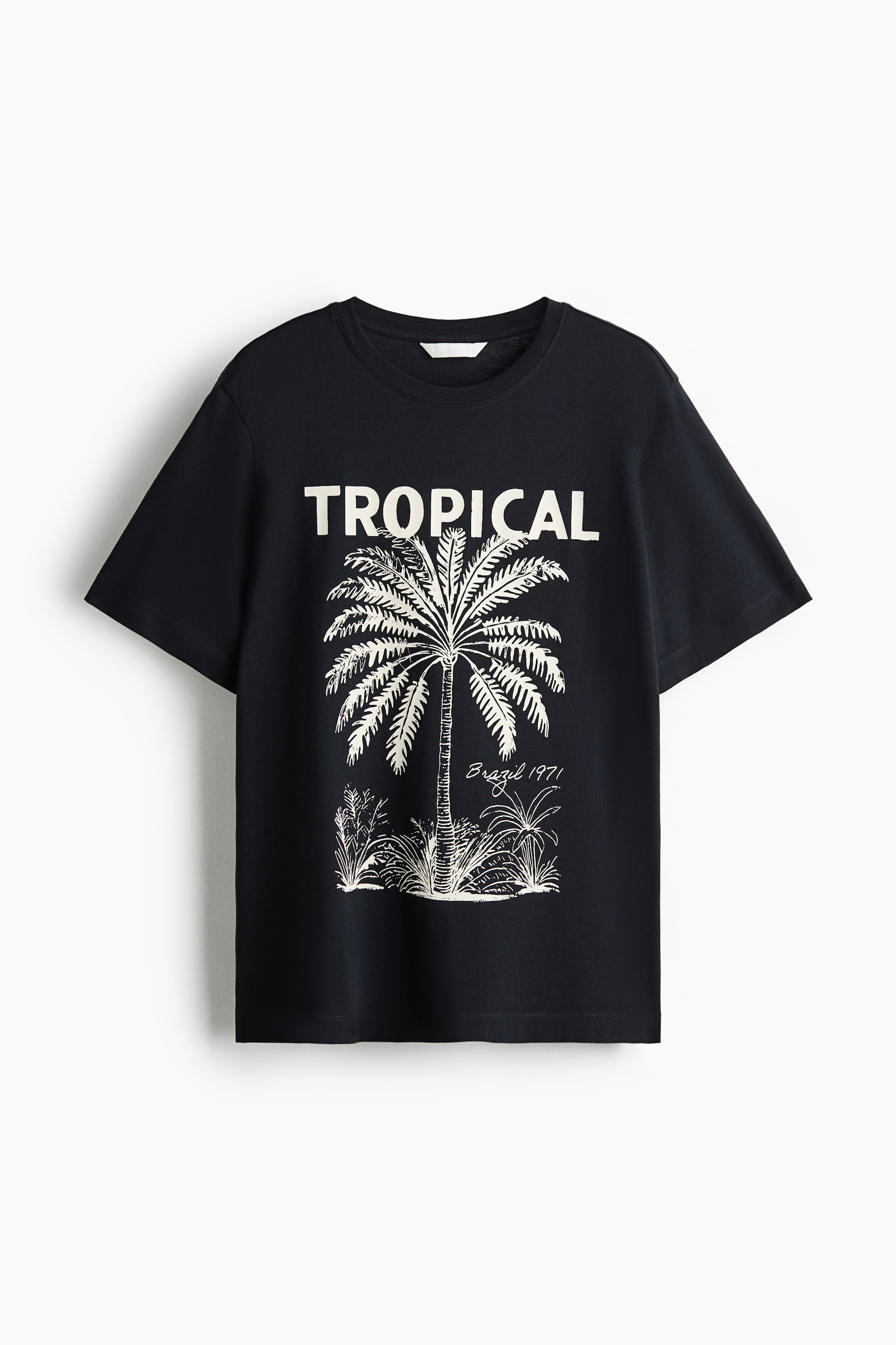 Voir une image plus grande: Un t-shirt classique en jersey de coton noir est posé à plat, face avant, arborant une impression "TROPICAL" en blanc. L'impression représente une illustration détaillée d'un palmier entouré de feuillage avec le texte 'Brésil 1971', tandis que le t-shirt est conçu avec un col rond et un ourlet droit.