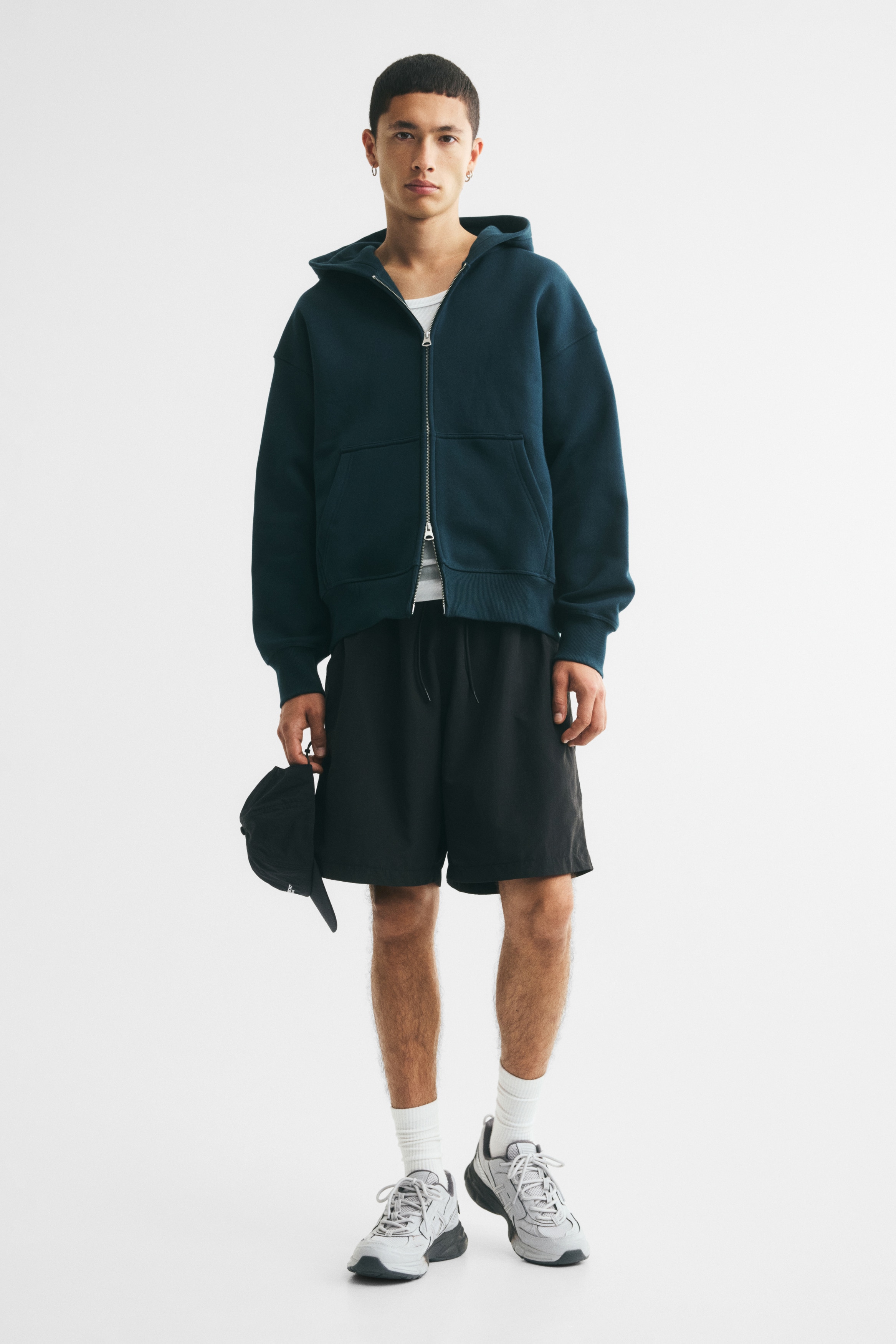 A dark teal zip-up hoodie showcases a relaxed fit from the front, boasting a full-length silver-toned zipper, a hood, a split kangaroo pocket, ribbed cuffs, and a ribbed hem.