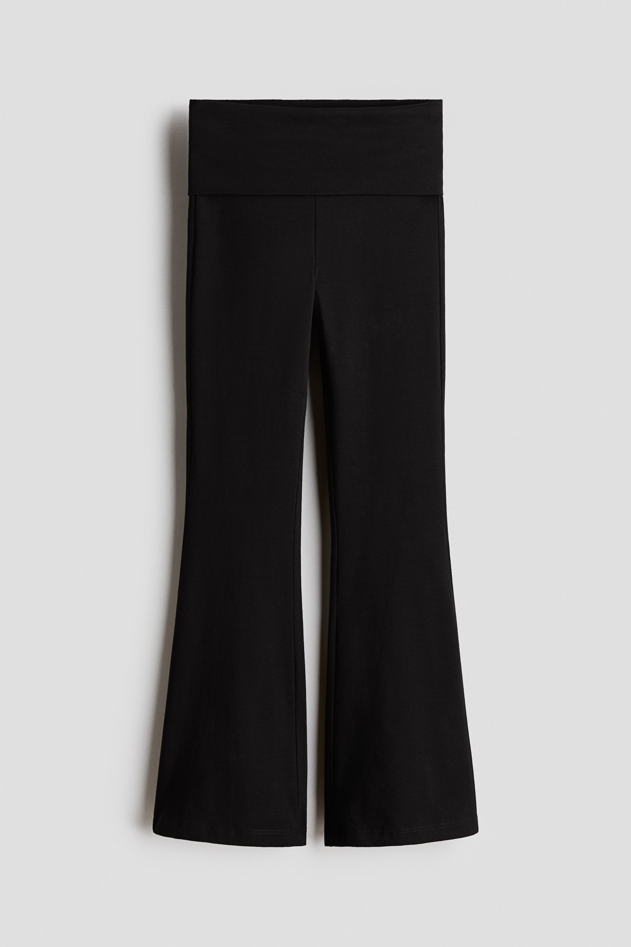 Zobrazit větší obrázek: Černé rozšířené legíny z měkkého bavlněného úpletu s širokým, překládacím pasem, které se vpředu prezentují, přiléhají přes stehna a rozšiřují se od kolen směrem k lemu.