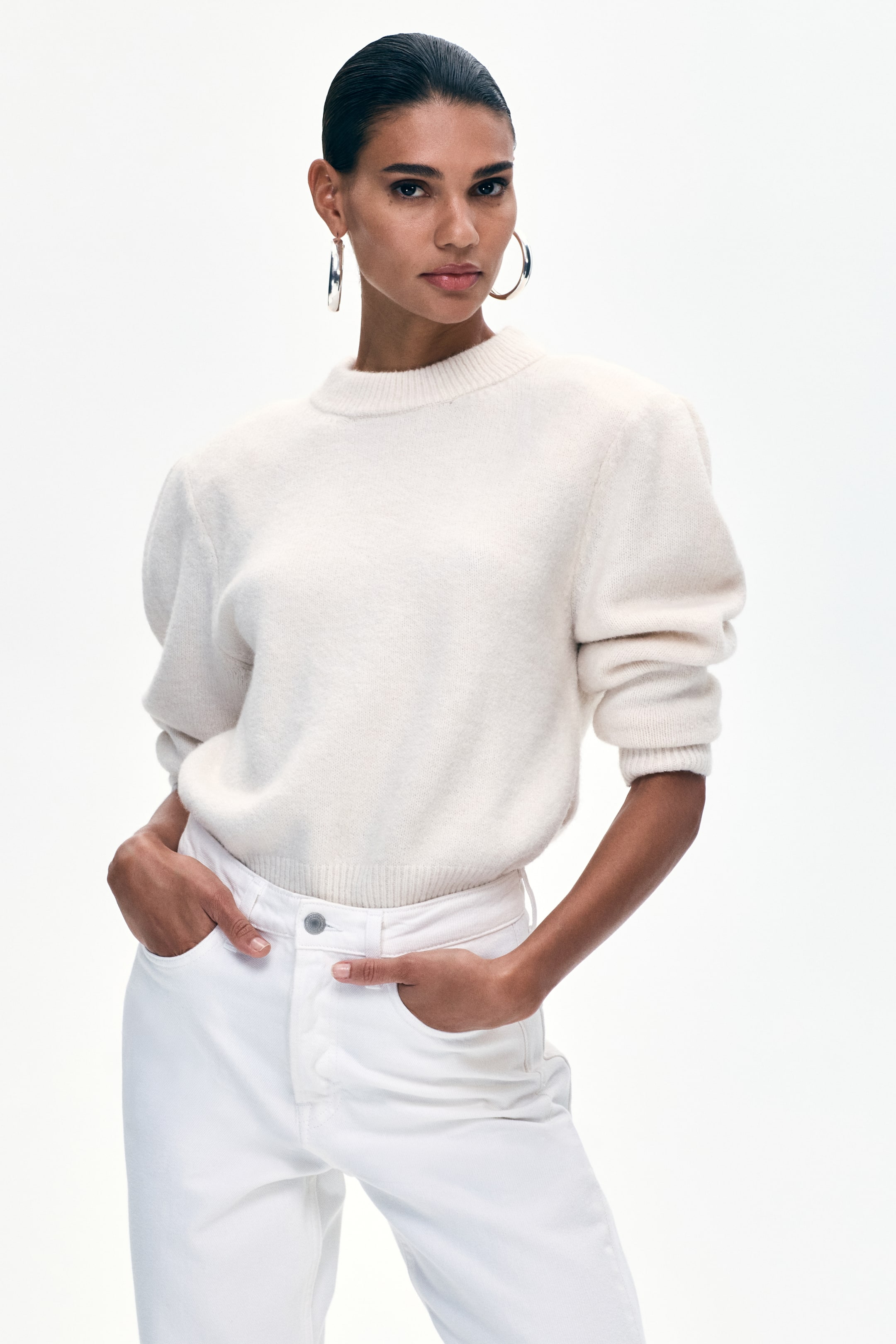 View larger image: An off-white mock neck jumper is showcased from a front angle, highlighting voluminous puff sleeves, ribbed cuffs, and a ribbed hem that is partially tucked into high-waisted white jeans.