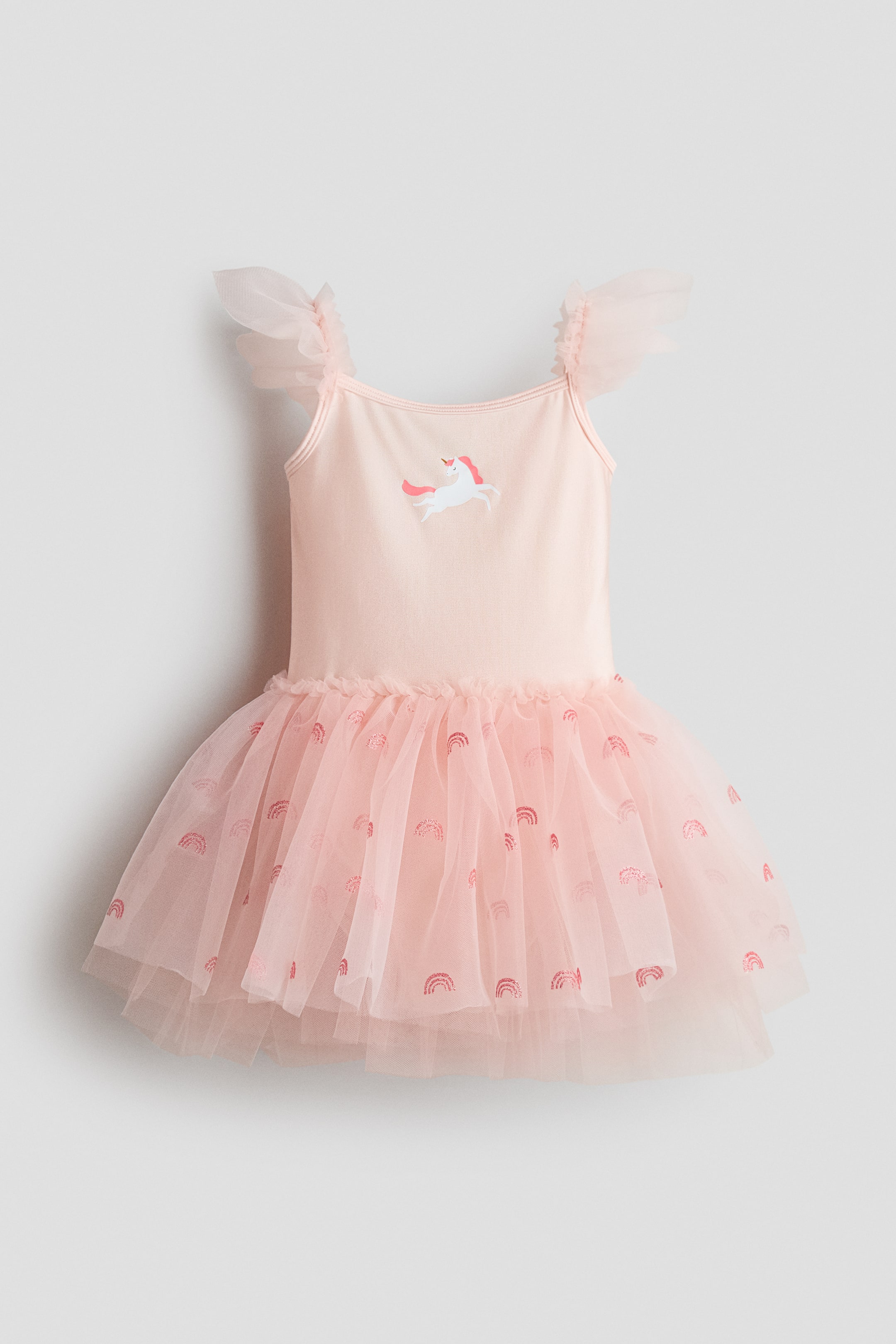 Ampliar la imagen: Se muestra un vestido de tutú infantil rosa claro desde el FRENTE, con un diseño de unicornio en el corpiño, mangas abullonadas de tul con volantes y una falda de tul en capas que exhibe motivos de arcoíris dispersos.