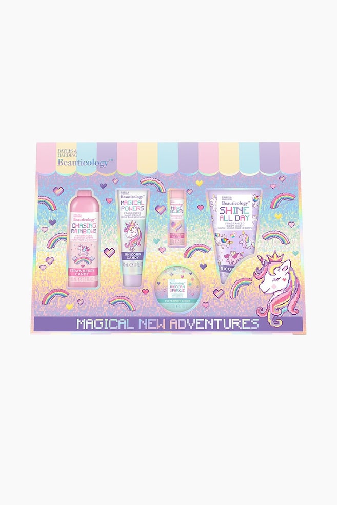Det Magical New Adventures gavesÃ¦t prÃ¦senterer en frontvendt visning af fem bade- og kropsprodukter arrangeret i en pastelfarvet Ã¦ske med pixelart-tema. Emballagen har et stribet markisedesign Ã¸verst og fremviser en shower creme, hÃ¥ndcreme, lÃ¦bepomade, badesalt og body wash dekoreret med pixelerede enhjÃ¸rninger, regnbuer og hjerter. - 1
