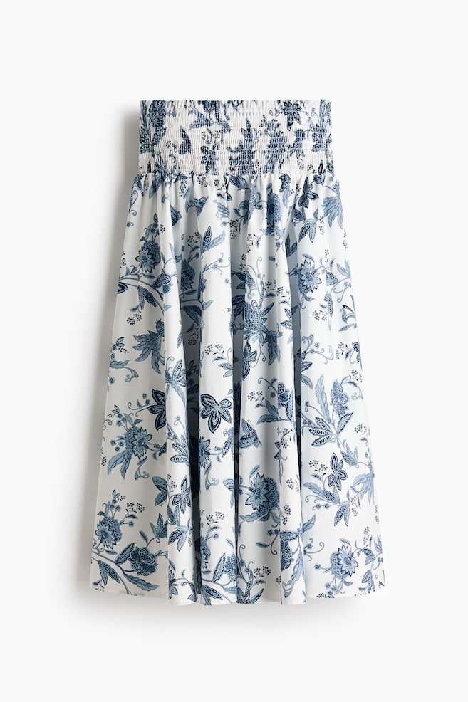 A white midi skirt is displaying a blue floral pattern from the front. It is featuring a shirred waistband and a gathered, flowing body. - 1