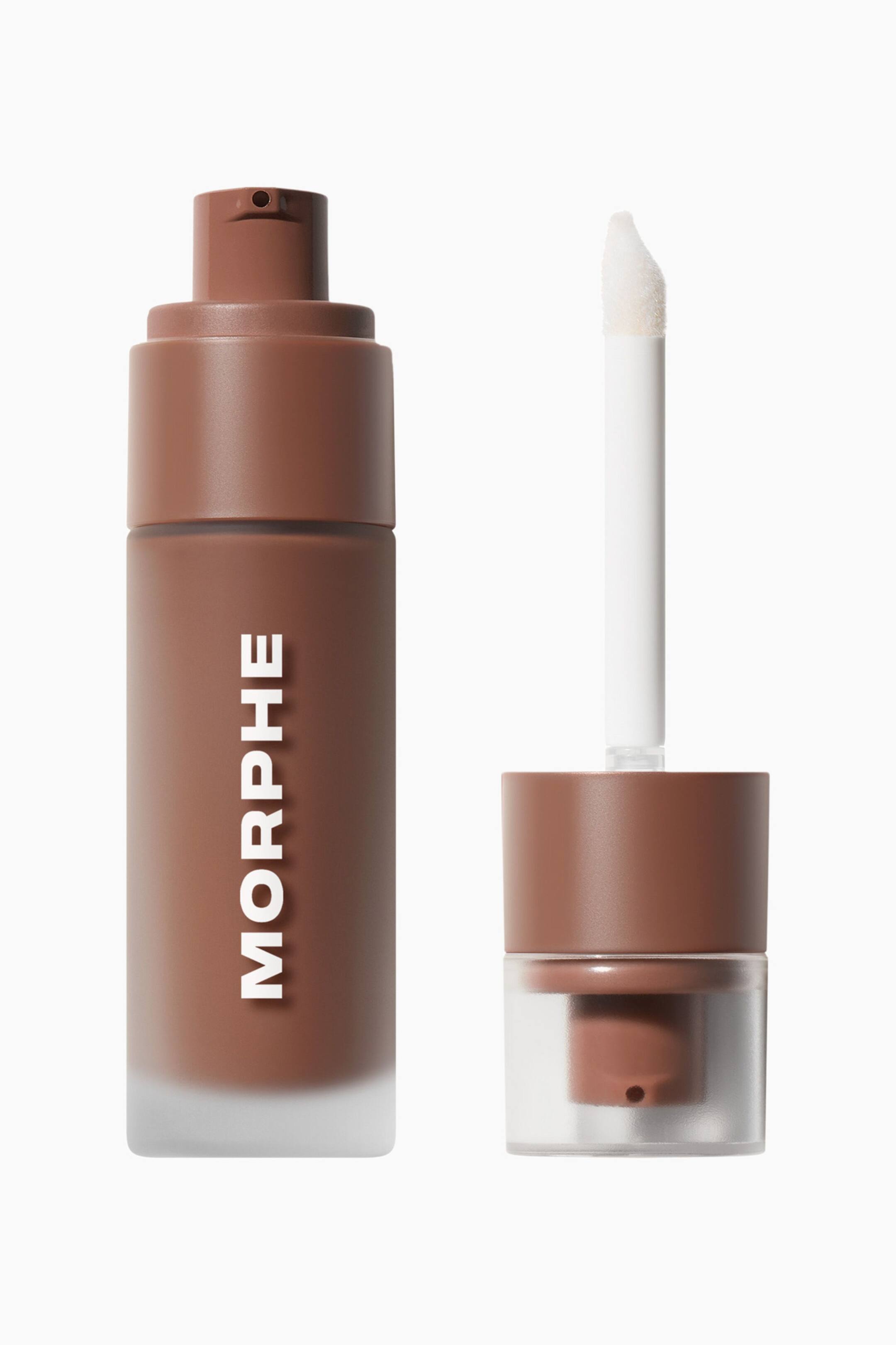 Vis større bilde: En frostet glassflaske med brun bronzer-væske står oppreist og viser vertikal hvit branding og en matchende brun pumpedyse på toppen. Ved siden av flasken står den avskrudde brune korken med klar base oppreist, med en lang hvit stav og en skrå doe-foot-applikatortupp som peker oppover.