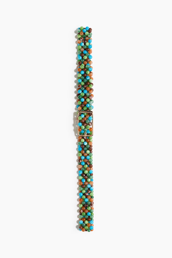 A belt is displayed from the front, forming a band with numerous small, round beads in varying shades of green, blue, brown, and light orange. A rectangular, metallic buckle with a central pin is positioned in the middle of the beaded band. - 1