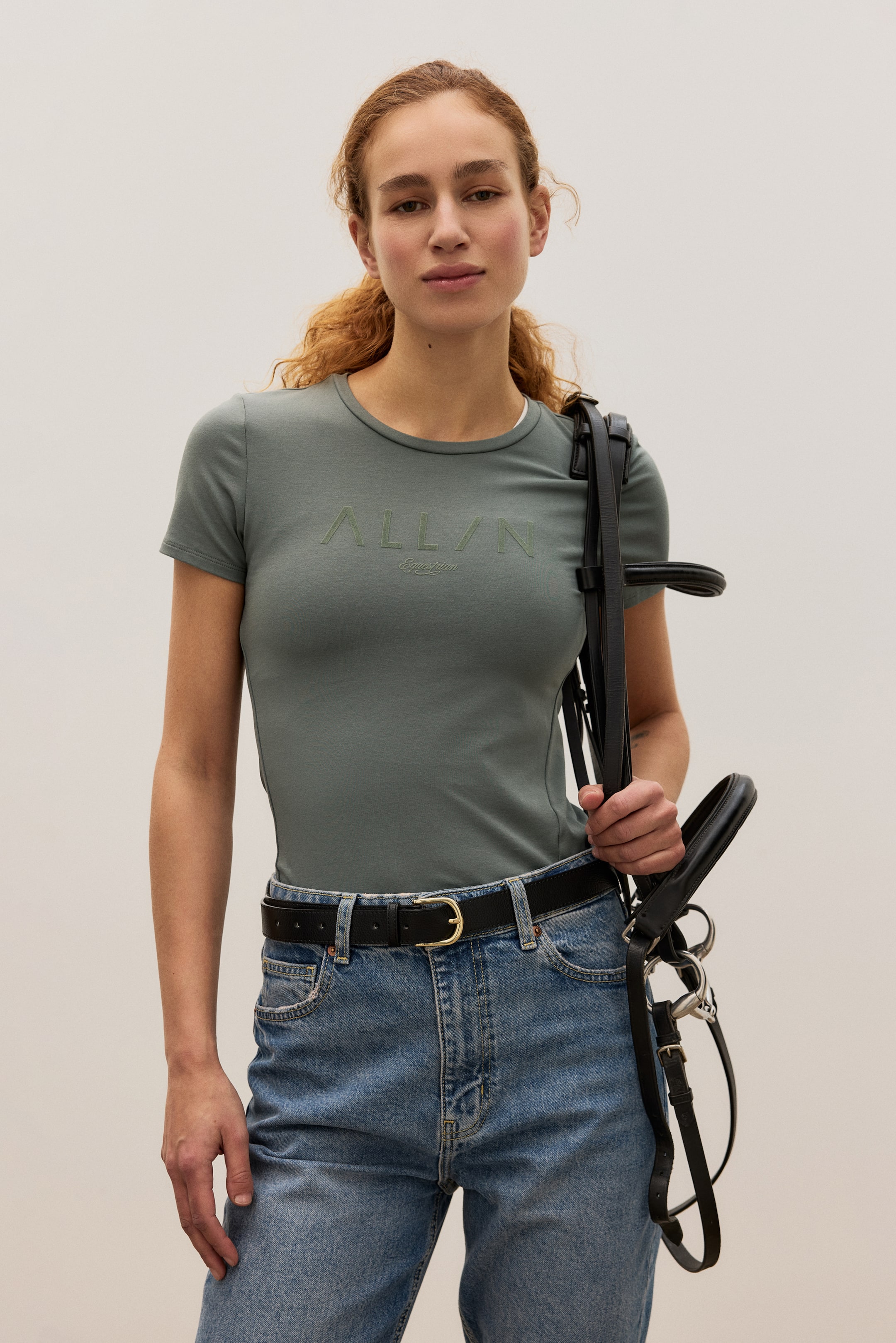 Größeres Bild ansehen: Ein salbeigrünes T-Shirt mit kurzen Ärmeln verfügt über einen Rundhalsausschnitt, den gestickten Schriftzug "ALL/N Equestrian" auf der Brust und eine figurbetonte Silhouette auf der Vorderseite.
