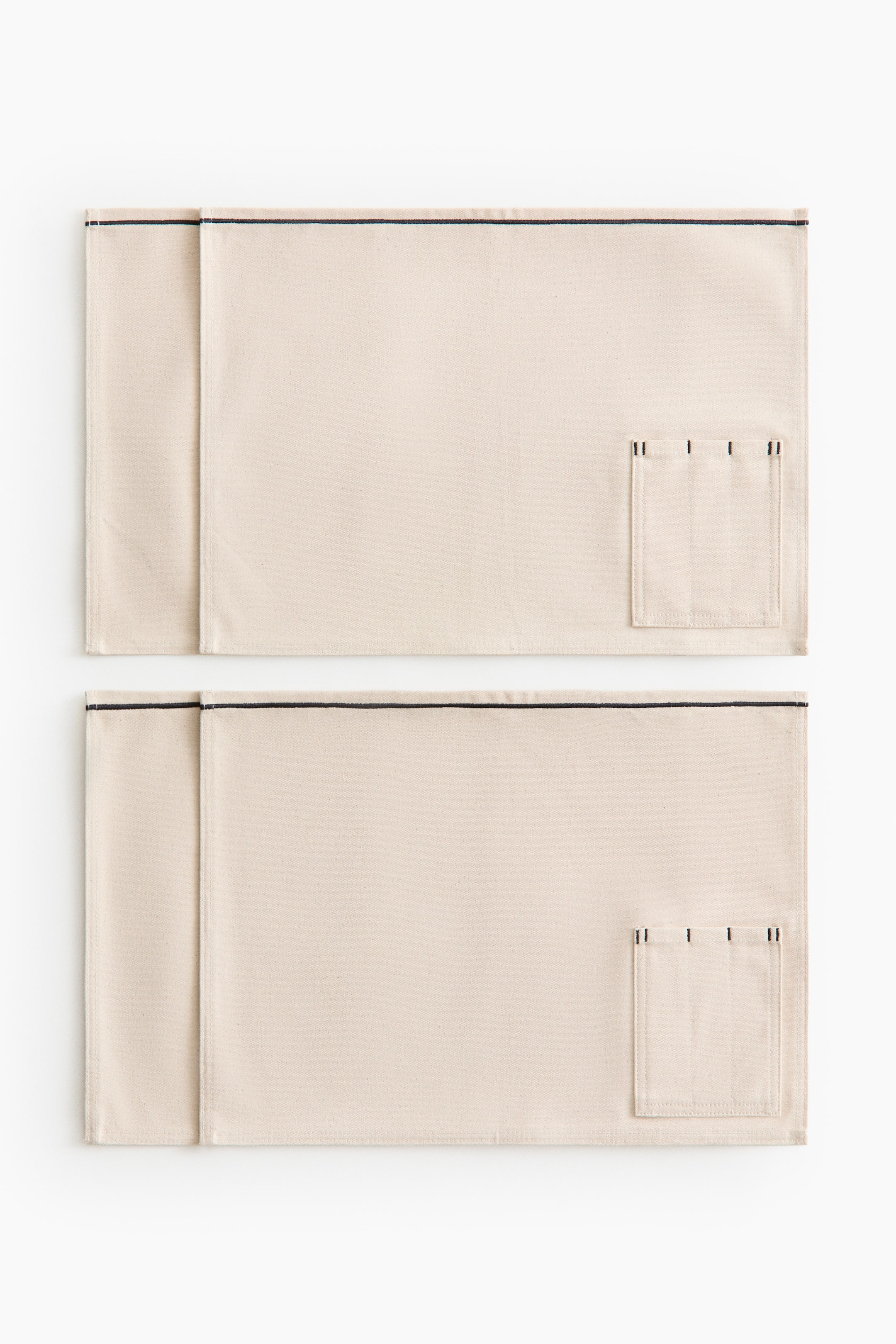 View larger image: Two rectangular light beige placemats are displayed from a front view, each showcasing a horizontal black stitched line along the top edge. On the right side of each placemat, a small rectangular patch pocket features three vertical black stitched divisions at its opening.