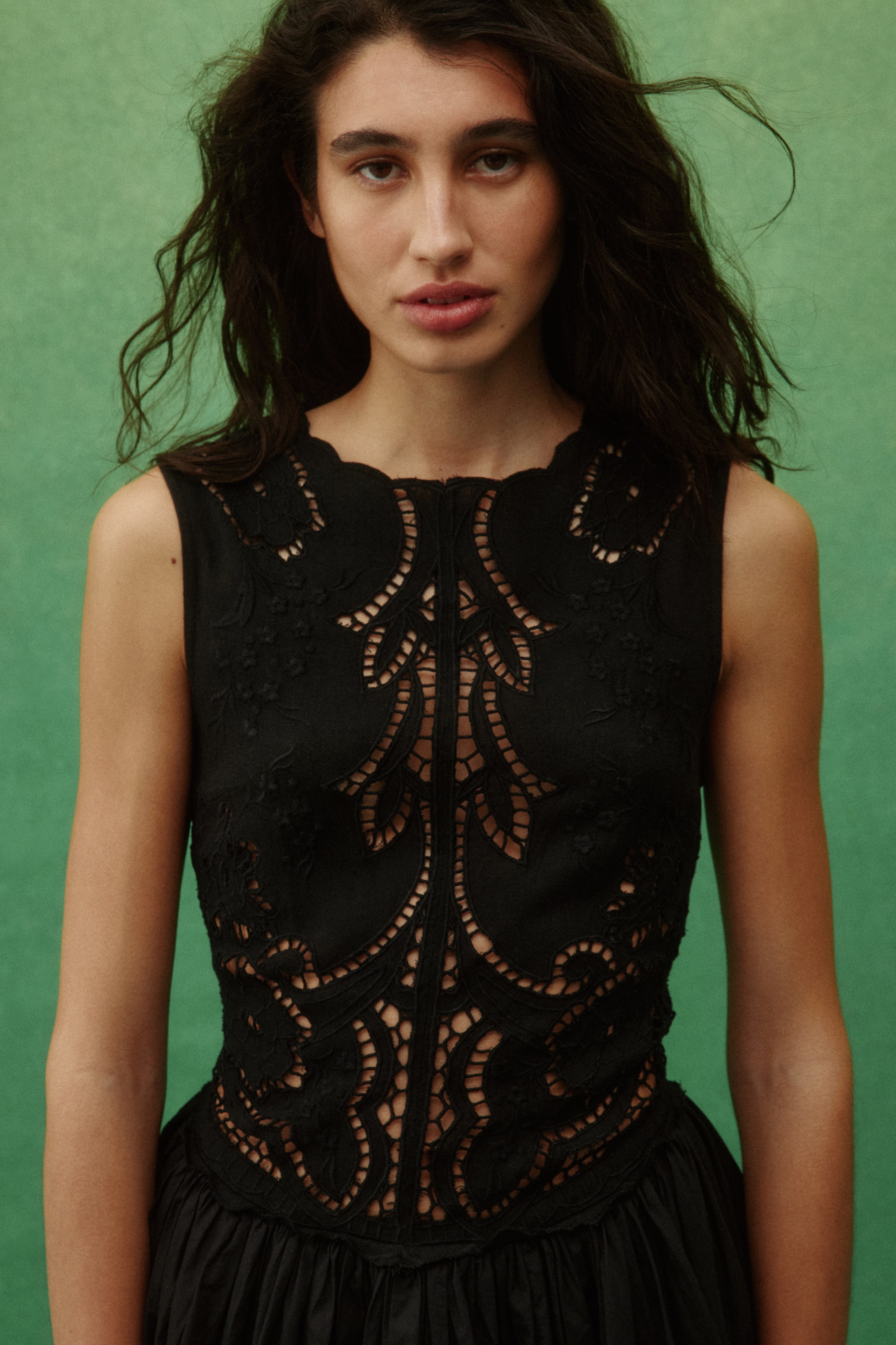 View larger image: A black sleeveless dress in woven fabric, featuring a fitted bodice with broderie anglaise detailing and a gathered skirt, is being worn by the model.