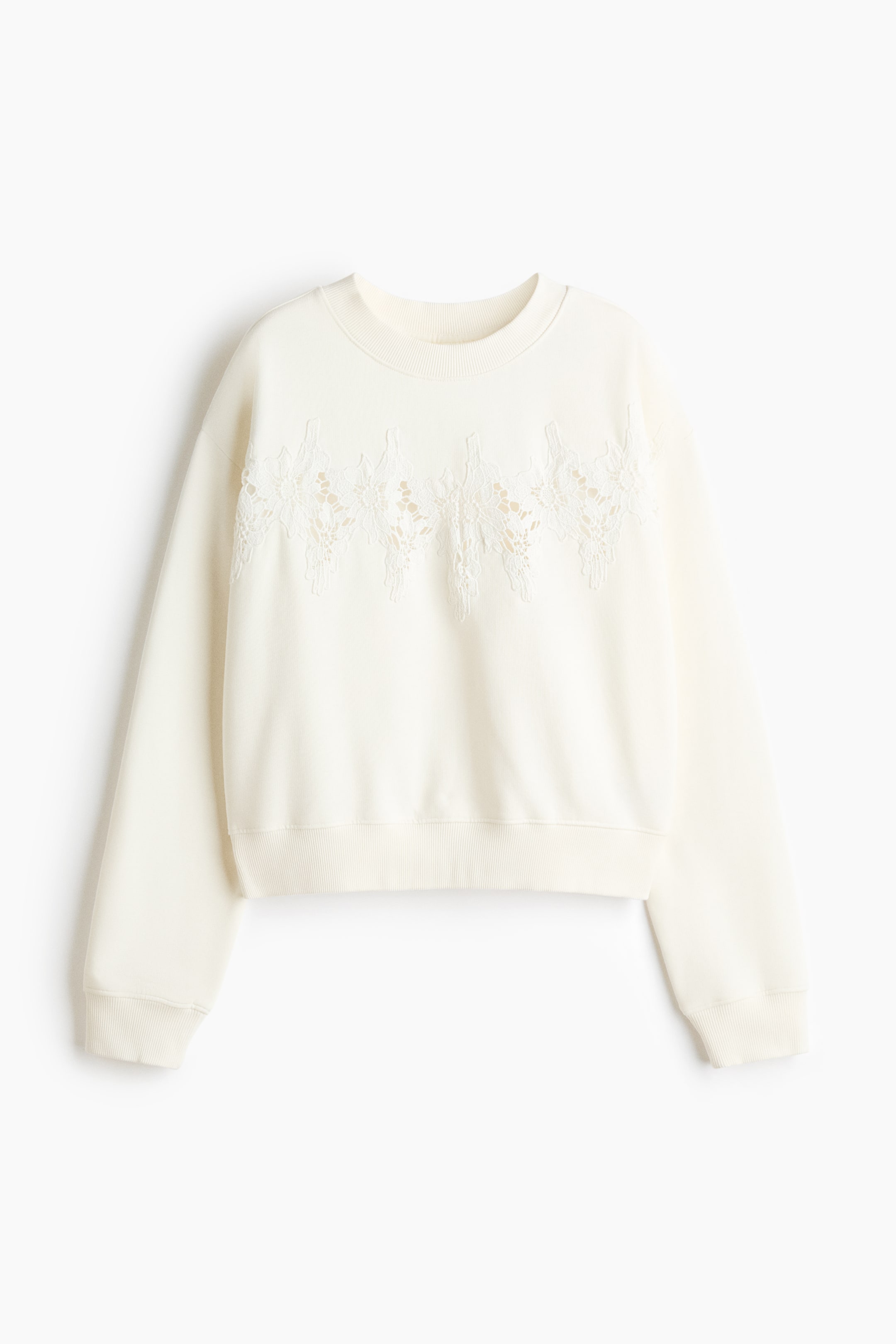 View larger image: A cream-coloured sweatshirt is shown from the front, featuring a ribbed crew neck, long sleeves with ribbed cuffs, and a ribbed hem. A band of intricate white lace applique runs across the upper chest, creating a decorative textured pattern.