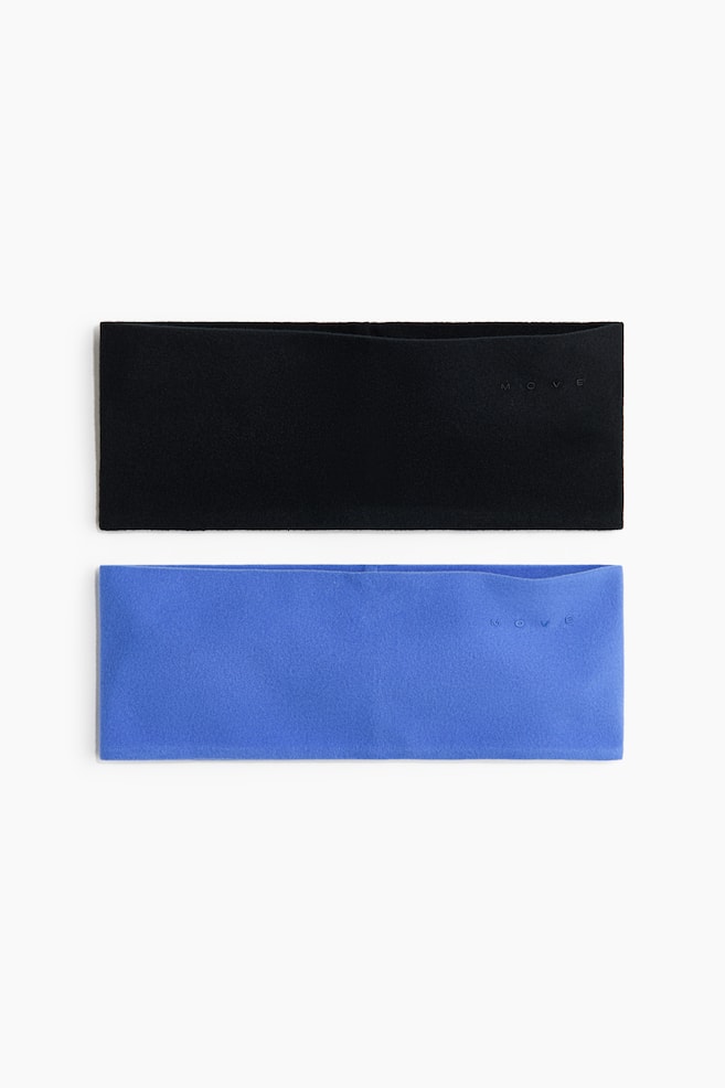 Two wide fleece headbands, one black and one blue, are laid flat in a front-facing view. Each headband features a contoured top edge and a small, subtly embossed "MOVE" logo on the right side. - 1