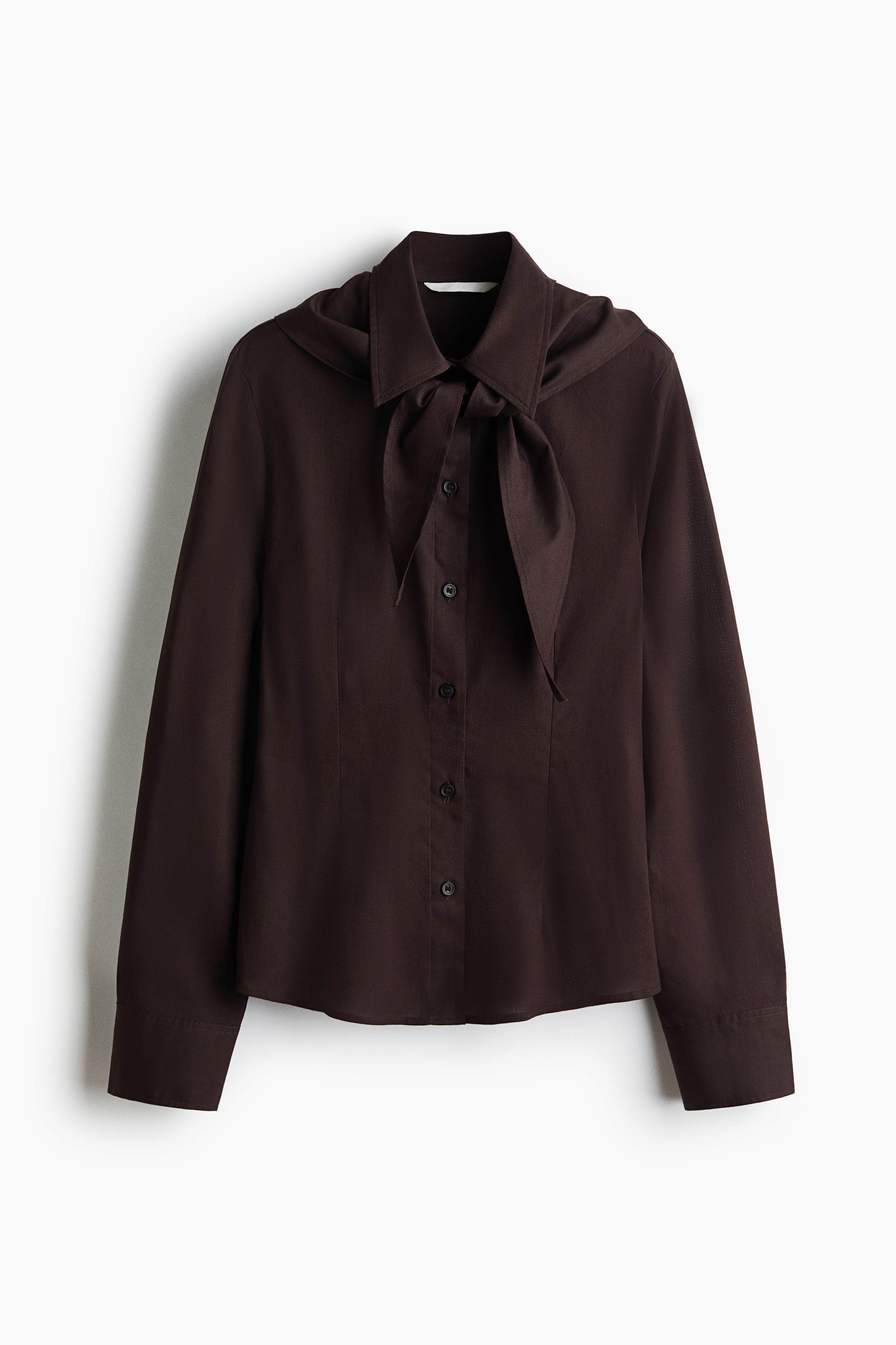 The model is wearing a dark brown cotton shirt featuring a pointed collar, a matching scarf tied at the neck, and a button-down front.