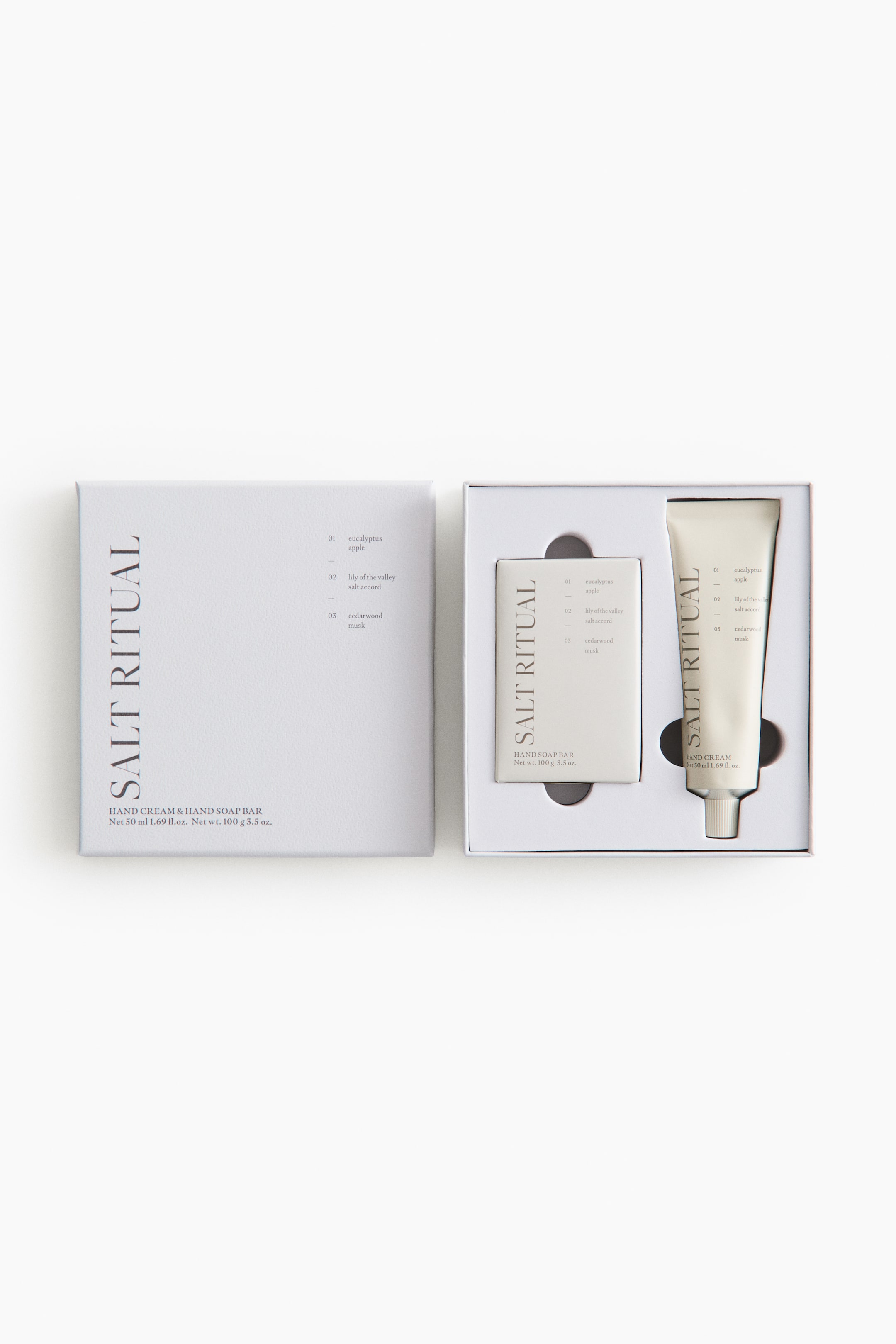 Ver imagen más grande: Un set de regalo blanco presenta una caja abierta, mostrando una pastilla de jabón rectangular y un tubo de crema de manos acomodados en su interior. Tanto la caja como los productos exhiben la marca vertical "SALT RITUAL", junto con descripciones de aromas y detalles del producto en sus superficies frontales.