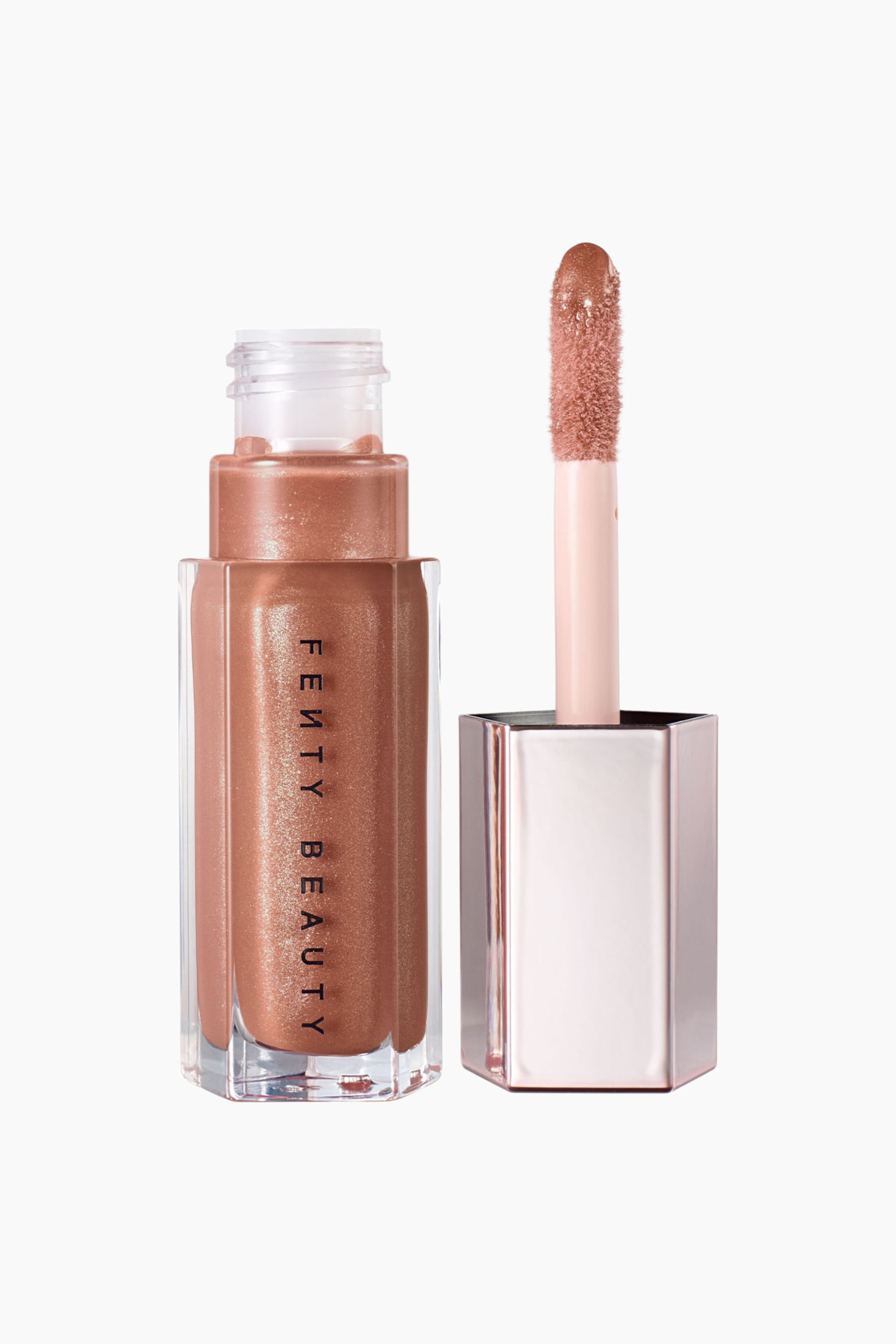Visa större bild: En öppen, sexkantig flaska med Fenty Beauty Gloss Bomb läppglans står bredvid sin upprätta applikatorstav. Den прозрачiga flaskan visar ett skimrande roséguldglans med varumärkesnamnet tryckt vertikalt, medan den metalliska roséguldfärgade korken håller staven med en glansbelagd doe-foot-applikator.