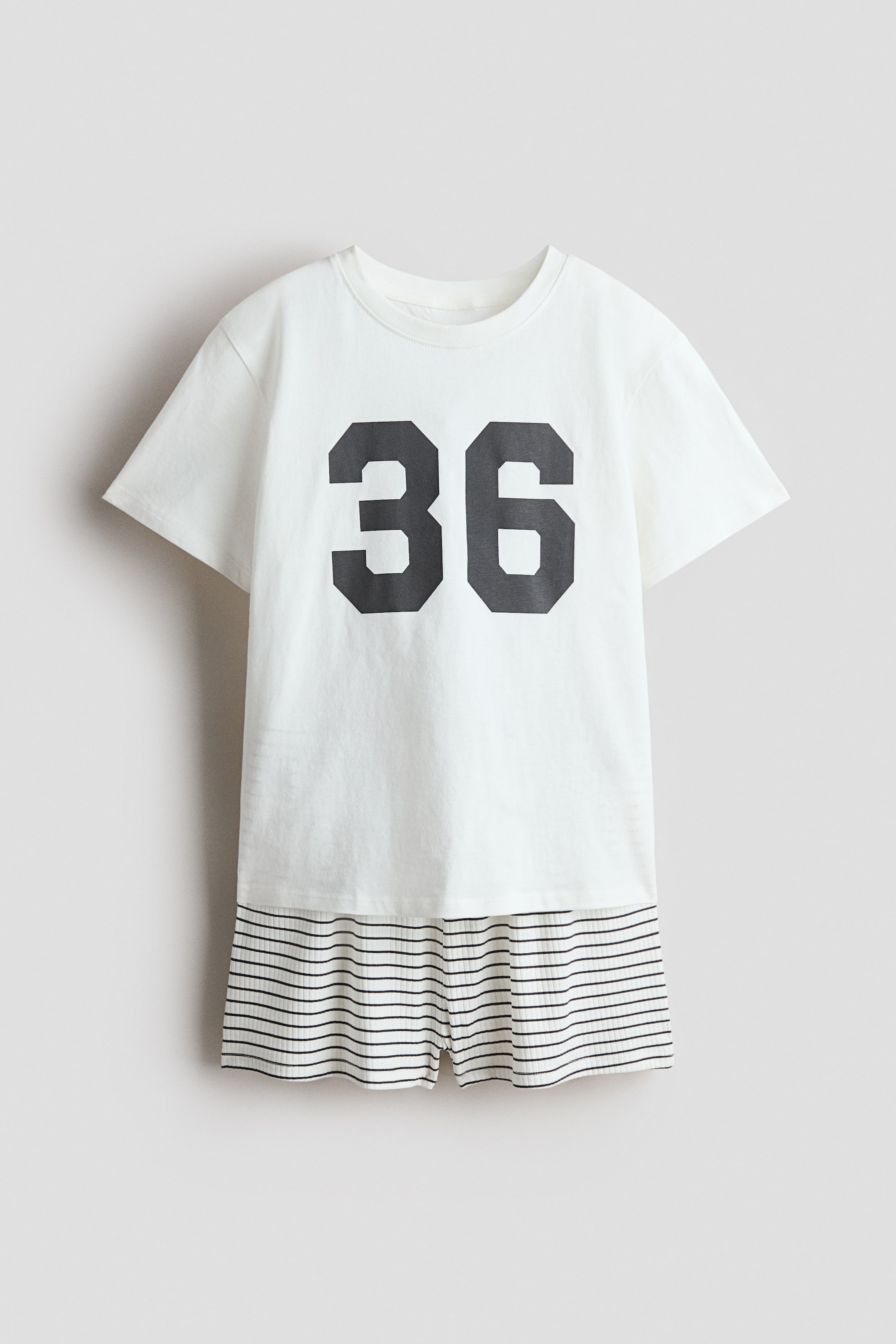 View larger image: Pyjamas showcase a white T-shirt from the front, boasting a prominent black "36" print, a round neckline, and a straight-cut hem. The T-shirt is paired with white shorts adorned with thin black horizontal stripes, a ribbed texture, and an elasticated waist.