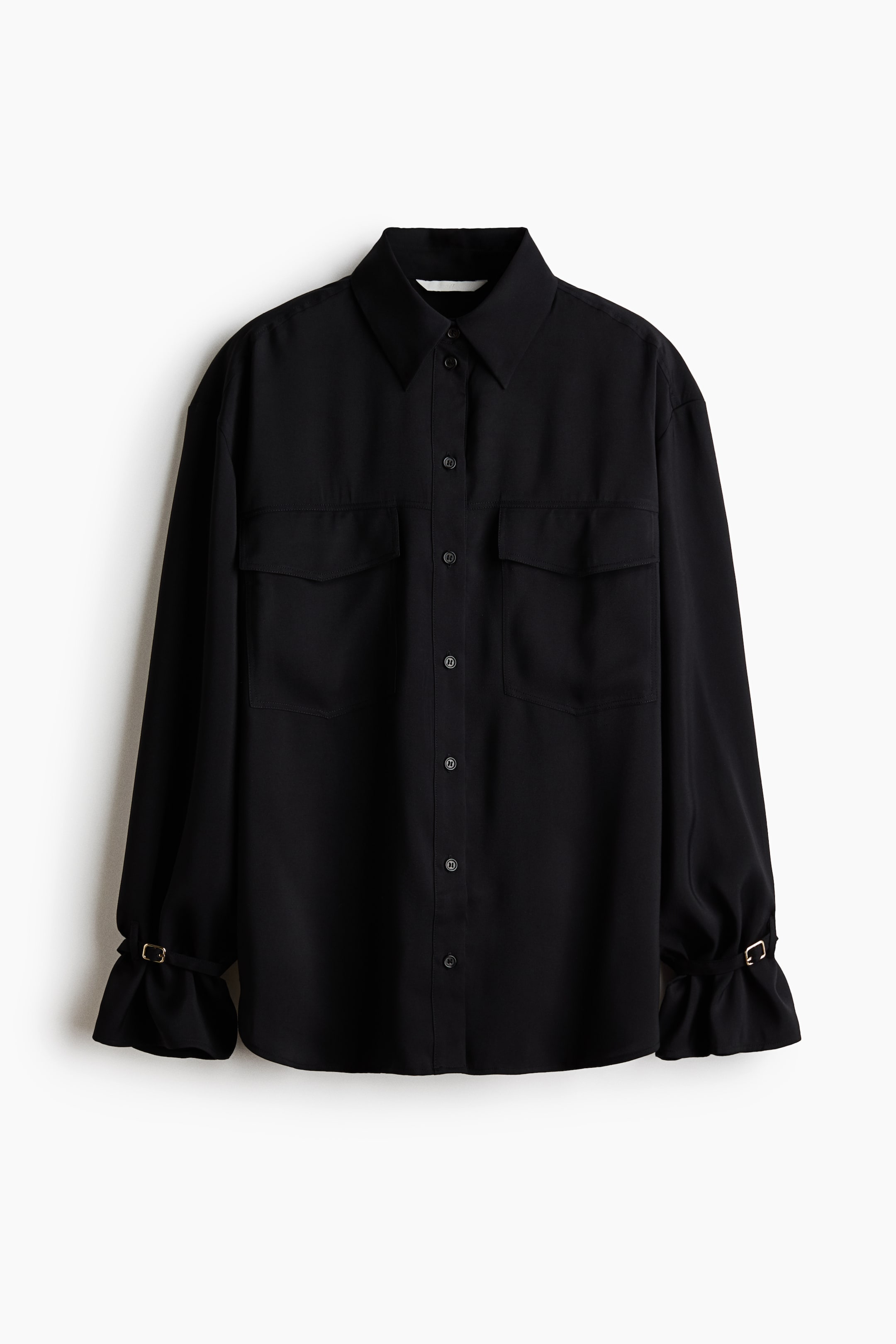 View larger image: A black button-down shirt is shown from the front, featuring a point collar, a central button placket, and two large chest flap pockets. The long sleeves end in gathered, ruffled cuffs secured by thin straps with small gold-toned buckles.