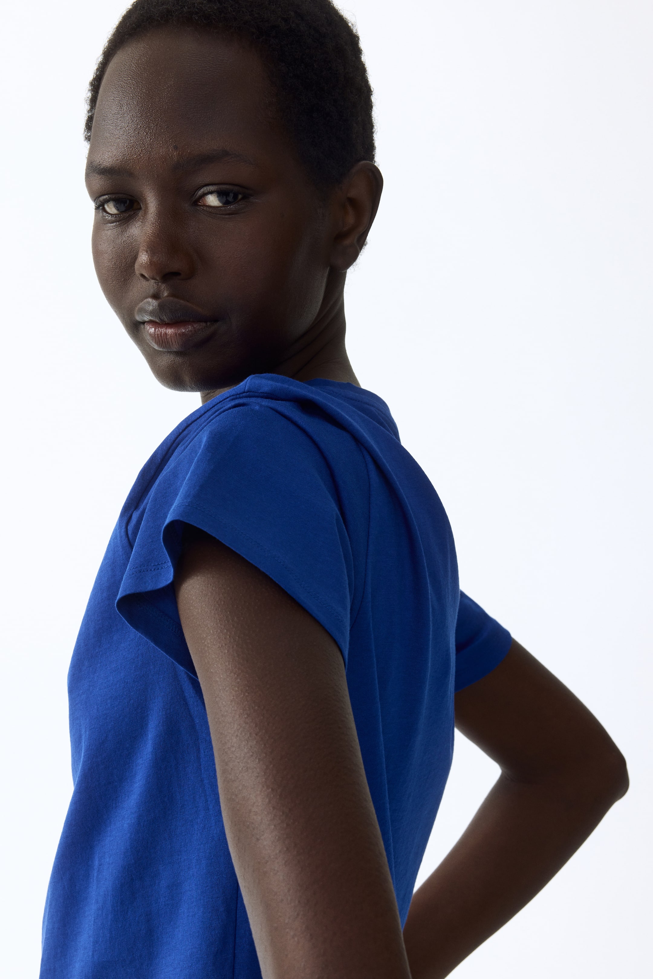 View larger image: "A vibrant blue top showcases short, draped sleeves with gentle folds, captured from a back-left perspective."