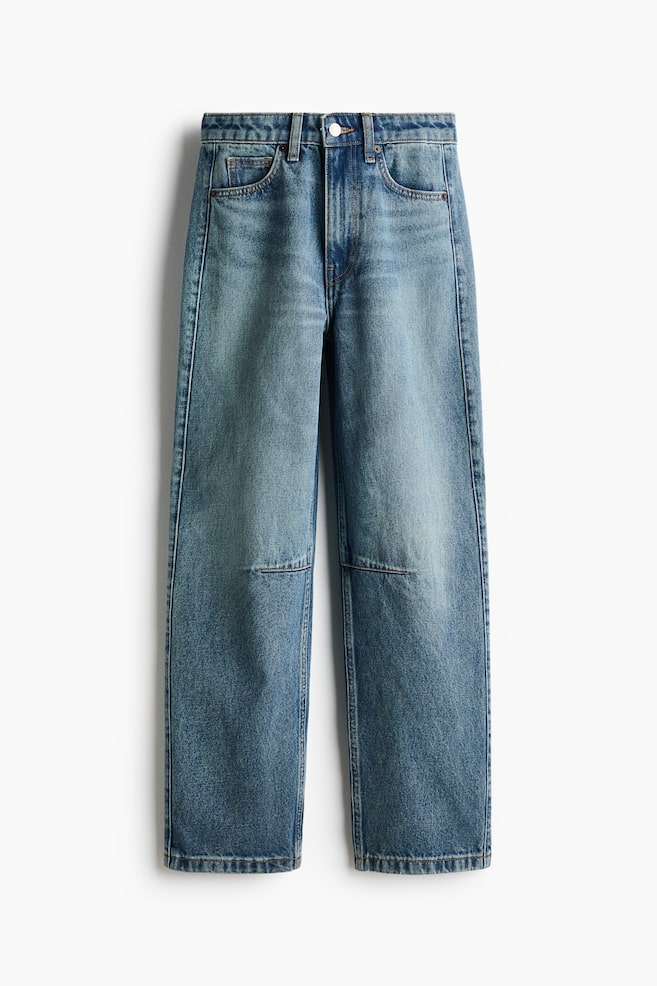 A front view of a pair of high-waisted, five-pocket jeans in a mid-blue wash is shown, featuring a zip fly with a button closure, belt loops, and curved, voluminous legs tapering toward the hems. The jeans are displaying subtle fading on the thighs and a horizontal seam detail across each knee. - 1
