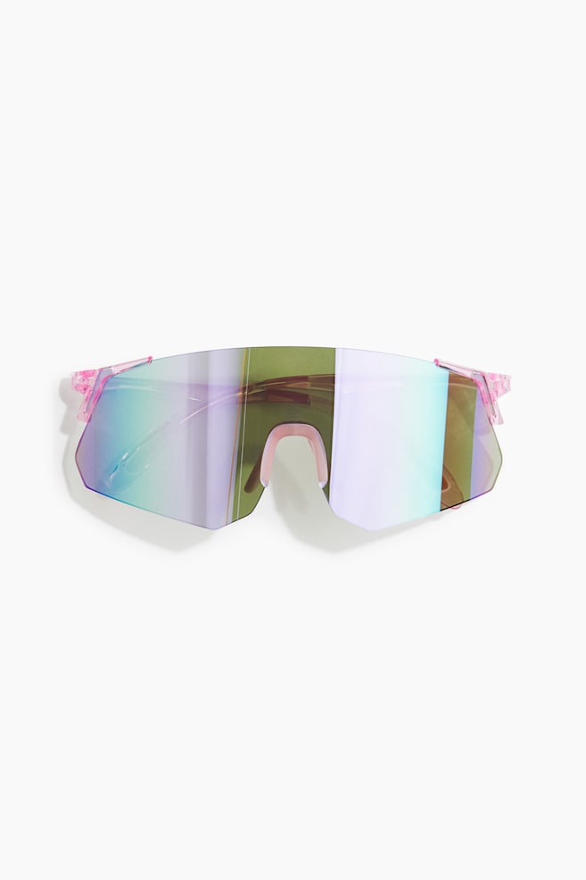 These activewear sunglasses, shown from the front, feature a continuous, rimless shield lens with a reflective, iridescent finish in shades of green, blue and purple. The sunglasses incorporate translucent pink polycarbonate temples and a matching pink nose pad. - 1