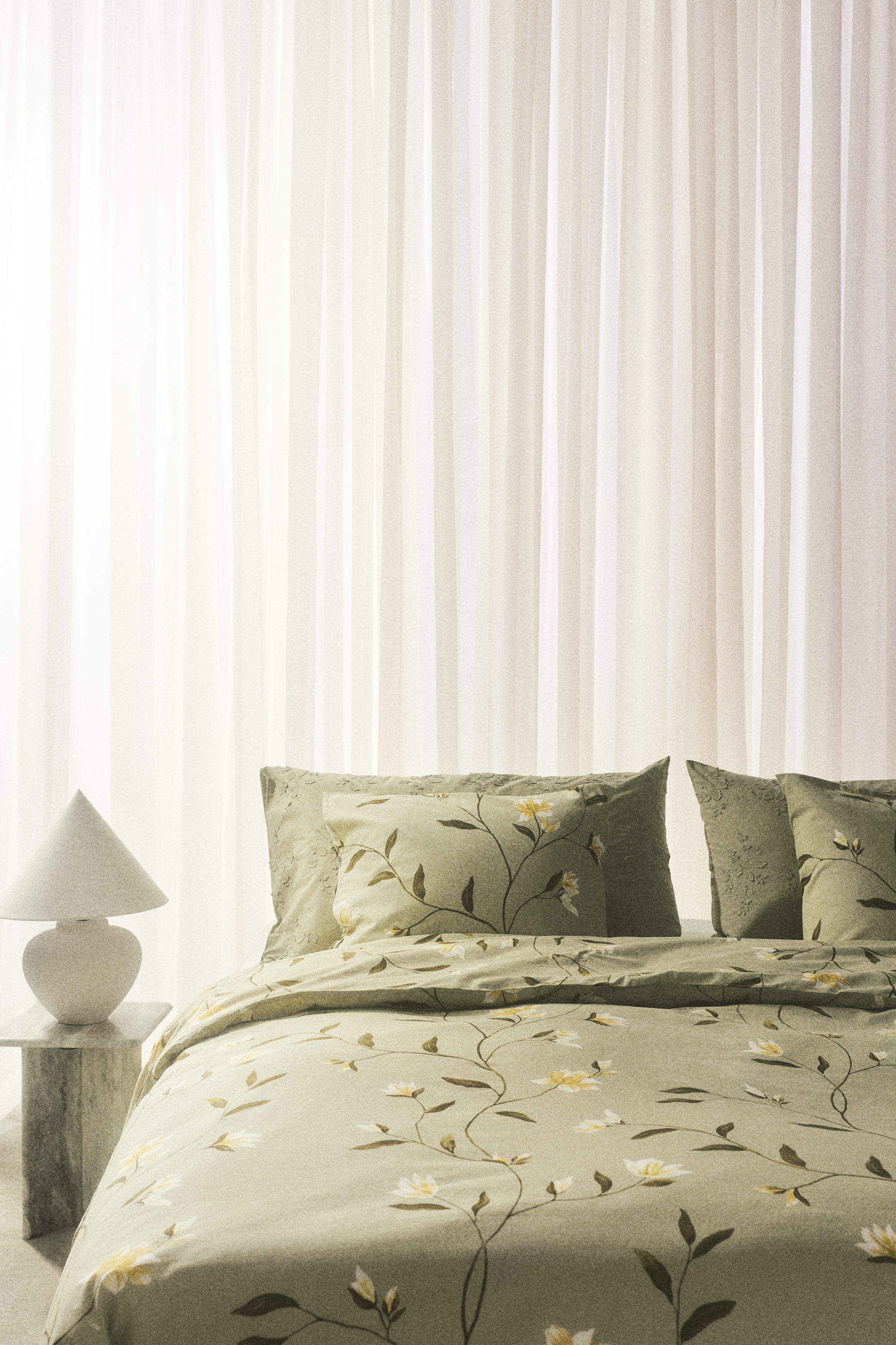 View larger image: "A light green duvet cover set showcases a floral pattern with winding dark green stems and soft yellow flowers spread across its woven fabric. The duvet cover elegantly drapes over a bed, accompanied by two matching pillowcases positioned upright at the head."