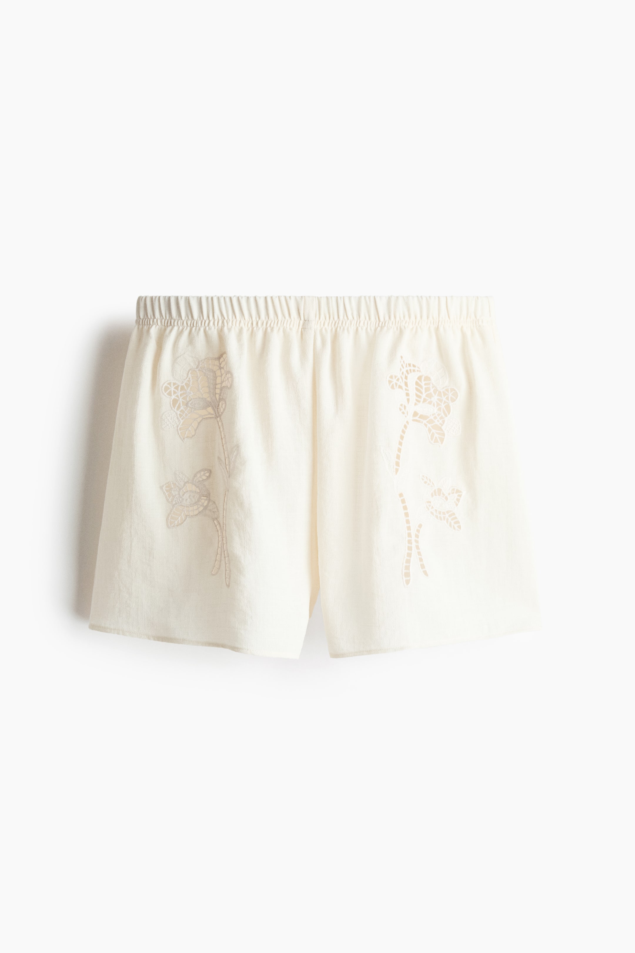 View larger image: The off-white woven shorts feature a loose fit, a regular elastic waistband, and flower-shaped broderie anglaise patterns on the front.