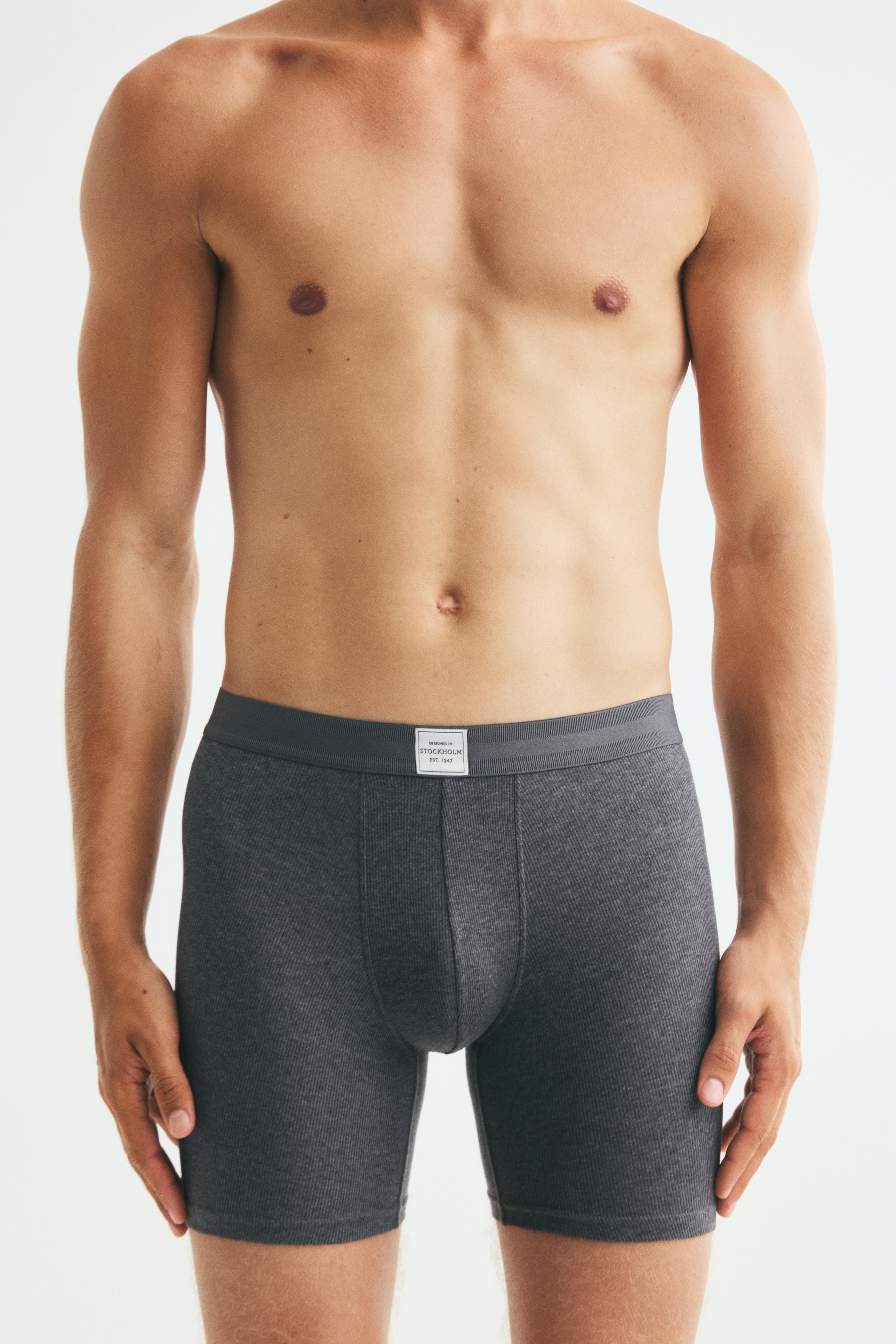Three pairs of menâs ribbed boxer briefs are stacked and facing front, showing a dark teal pair at the back, a black pair in the middle, and a heather grey pair in the front. Each pair features a tonal elastic waistband with a small, white rectangular brand label centred on the front.
