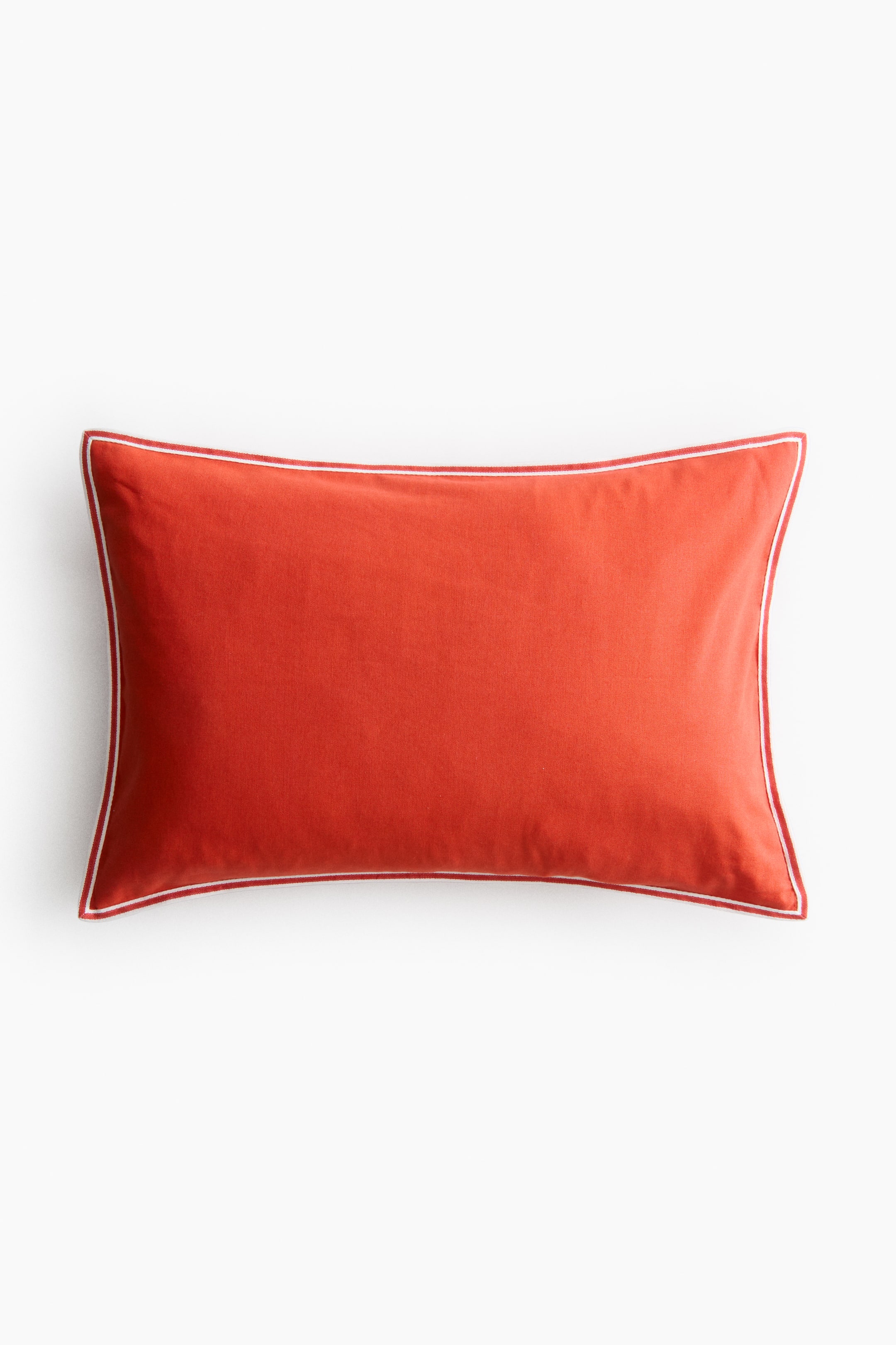 View larger image: A rectangular pillow is facing front, featuring an orange-red colour with white piping outlining its perimeter.