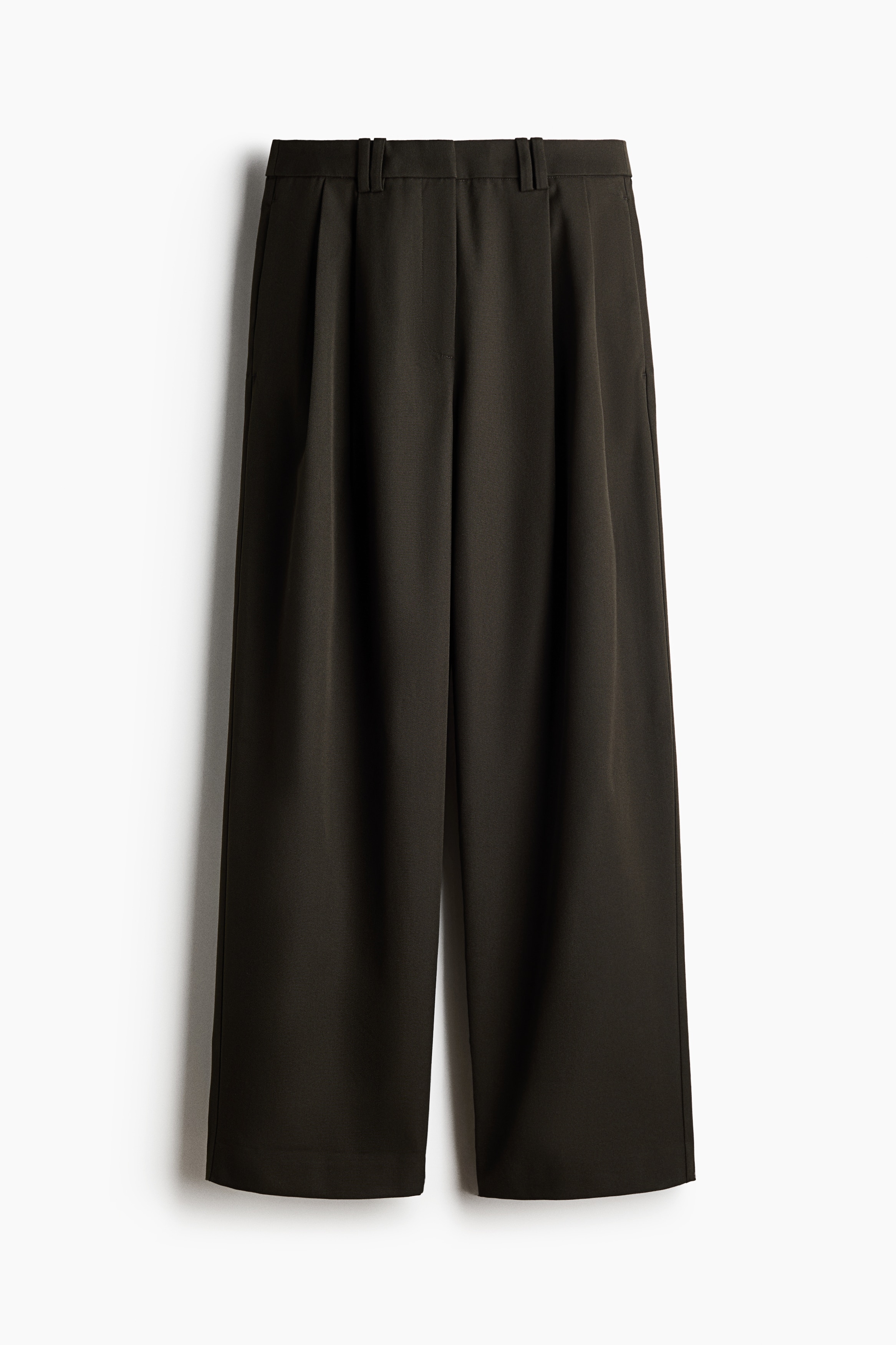 Loose-fit, wide-leg pants in dark olive green woven fabric are worn by the model, who is standing with hands tucked into the side pockets. The pants feature front pleating and are styled with a black leather belt with a decorative gold buckle and a tucked-in black sweater.