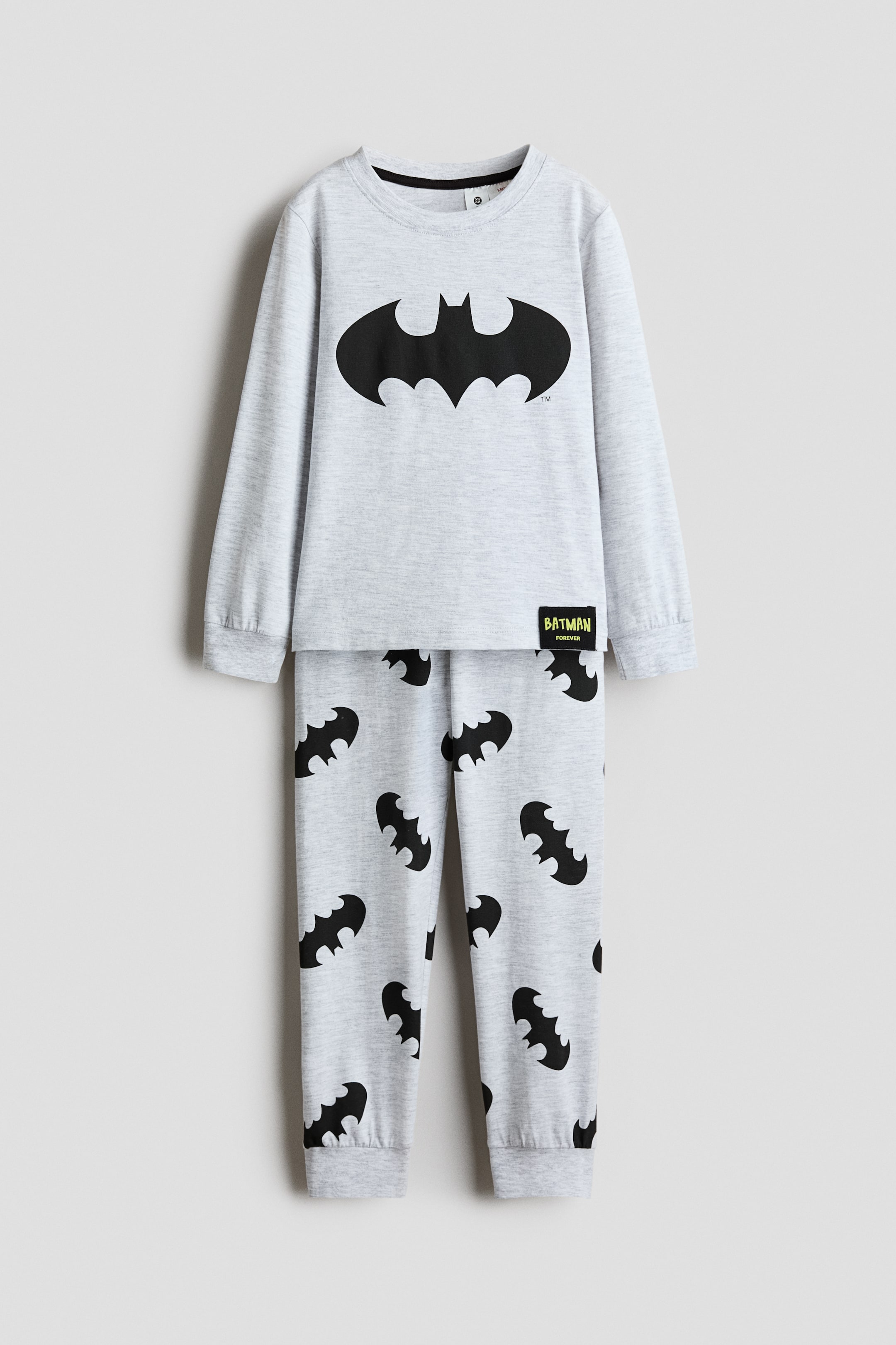 View larger image: Light grey cotton jersey pyjamas feature a top with a large black Batman logo on the front, a black 'Batman Forever' label near the hem, a round ribbed neckline, long sleeves, and ribbed cuffs. The matching bottoms feature an all-over print of smaller black Batman logos and ribbed hems.