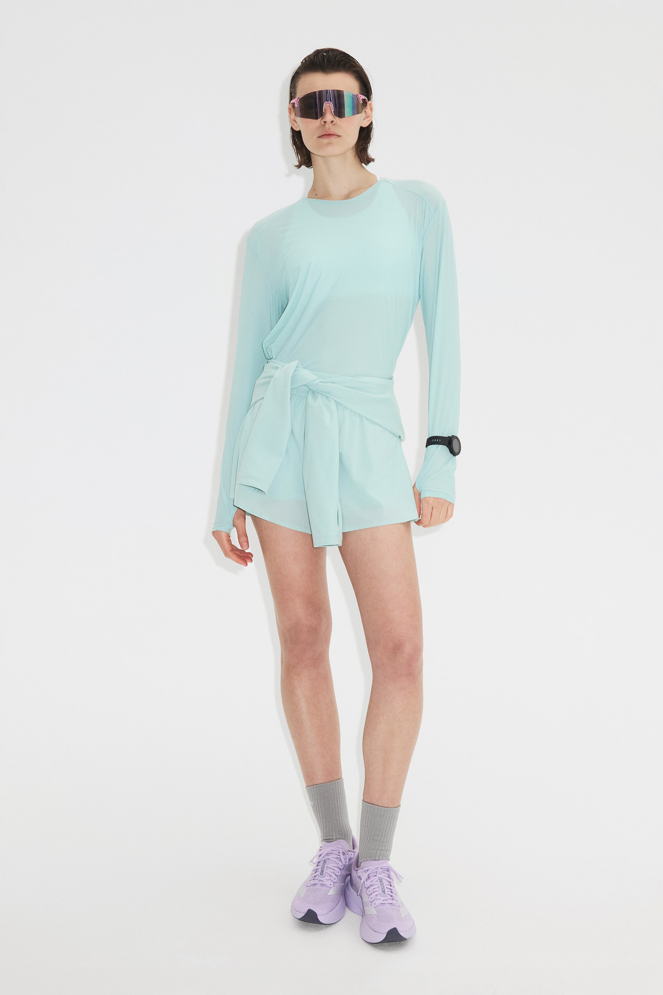 הצגת תמונה גדולה יותר: חולצה ארוכה בצבע אקווה בהיר נלבשת עם מכנסיים קצרים תואמים. החולצה הקלה מתאפיינת בצווארון עגול ושרוולים בסגנון רגלן, כאשר החלק התחתון שלה כרוך ונקשר במותן מעל המכנסיים הרחבים.