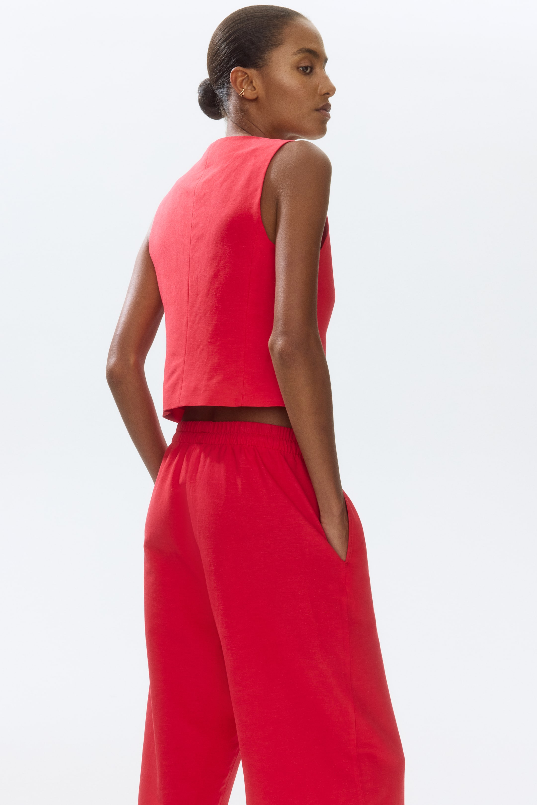 View larger image: A red sleeveless top featuring a high neckline, cropped hem, and a visible back seam is paired with matching red wide-leg pants that showcase an elasticated waistband and side pockets. The ensemble is presented from a back-side angle.