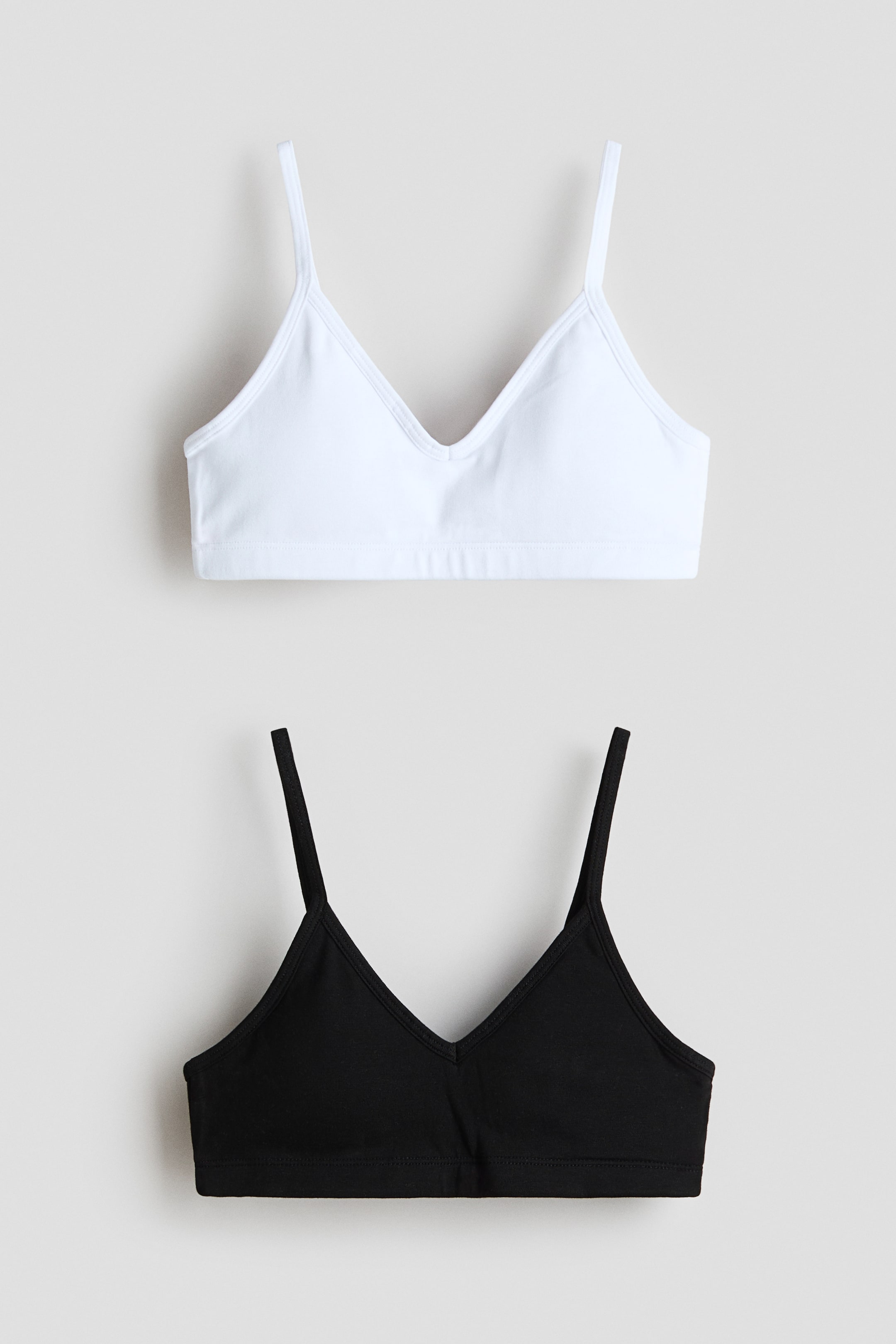 View larger image: Displayed are two bralettes, one in white and the other in black, each showcasing thin spaghetti straps, a V-neckline, and a wide underband from a front perspective.
