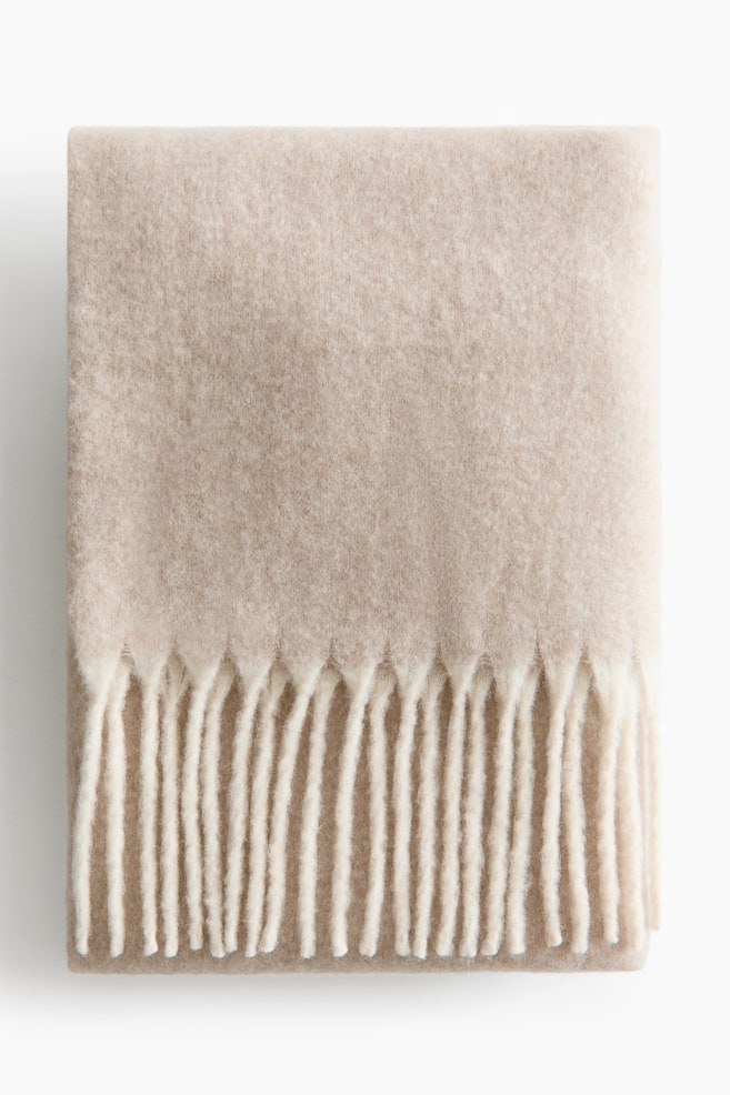 A light beige blanket is folded neatly into a rectangular shape, showcasing a soft, brushed texture across its surface. A contrasting cream-coloured fringe is visible along the bottom edge of the folded blanket. - 1