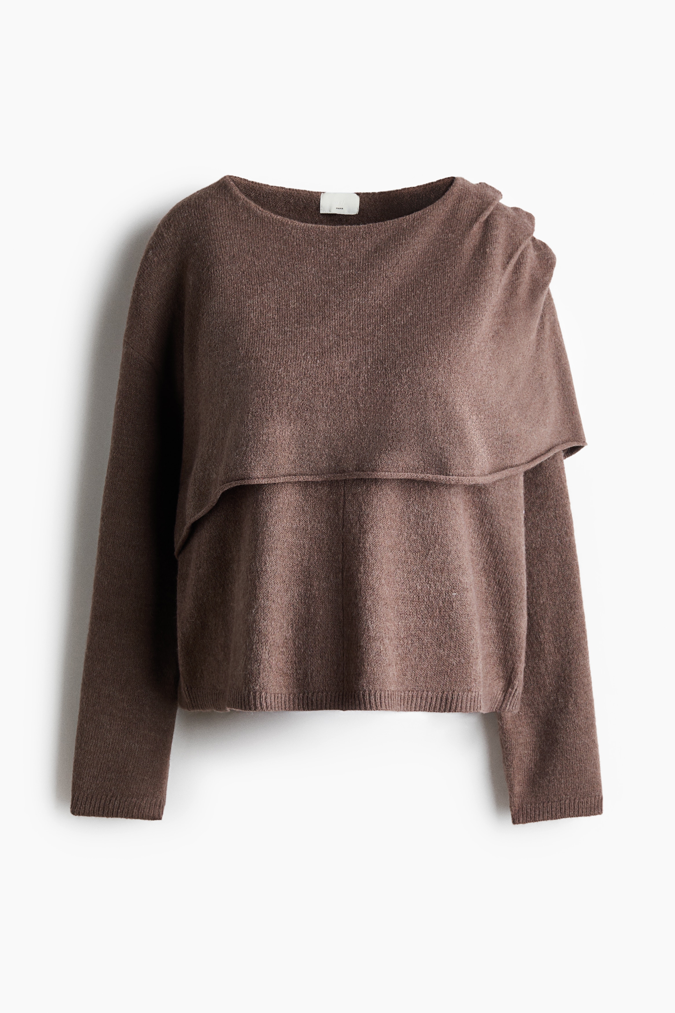 Ein locker geschnittener brauner Strickpullover wird vom Model getragen und verfÃ¼gt Ã¼ber einen Rundhalsausschnitt, Ã¼berschnittene Schultern sowie eine asymmetrische obere Lage mit gerolltem Saum, die Ã¼ber eine Schulter fÃ¤llt. Der Pullover wird mit einer weiÃen Hose kombiniert, wÃ¤hrend das Model mit einer Hand in der HÃ¼fte posiert.