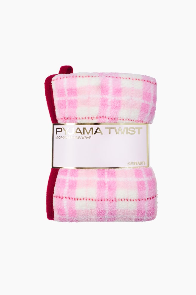 The microfiber hair wrap is shown from the front, featuring a pink and white plaid pattern in a soft, plush fabric with a dark pink trim. It is secured in the middle with a light pink paper band displaying the gold text "PYJAMA TWIST" and "MICROFIBER HAIR WRAP." - 1