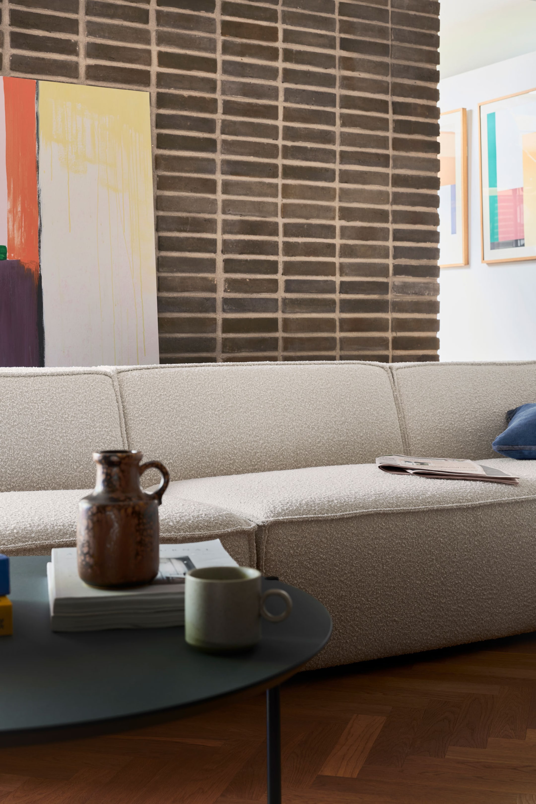 Größeres Bild anzeigen: Ein niedriges modulares Sofa, bezogen mit einem strukturierten Bouclé-Stoff in Off-White, ist nach rechts ausgerichtet und präsentiert seine klarlinigen, abgerundeten Kissen. Das Sofa zeigt Paspelnaht-Details entlang der Kanten seiner weichen Sitz- und Rückenlehnenbereiche.
