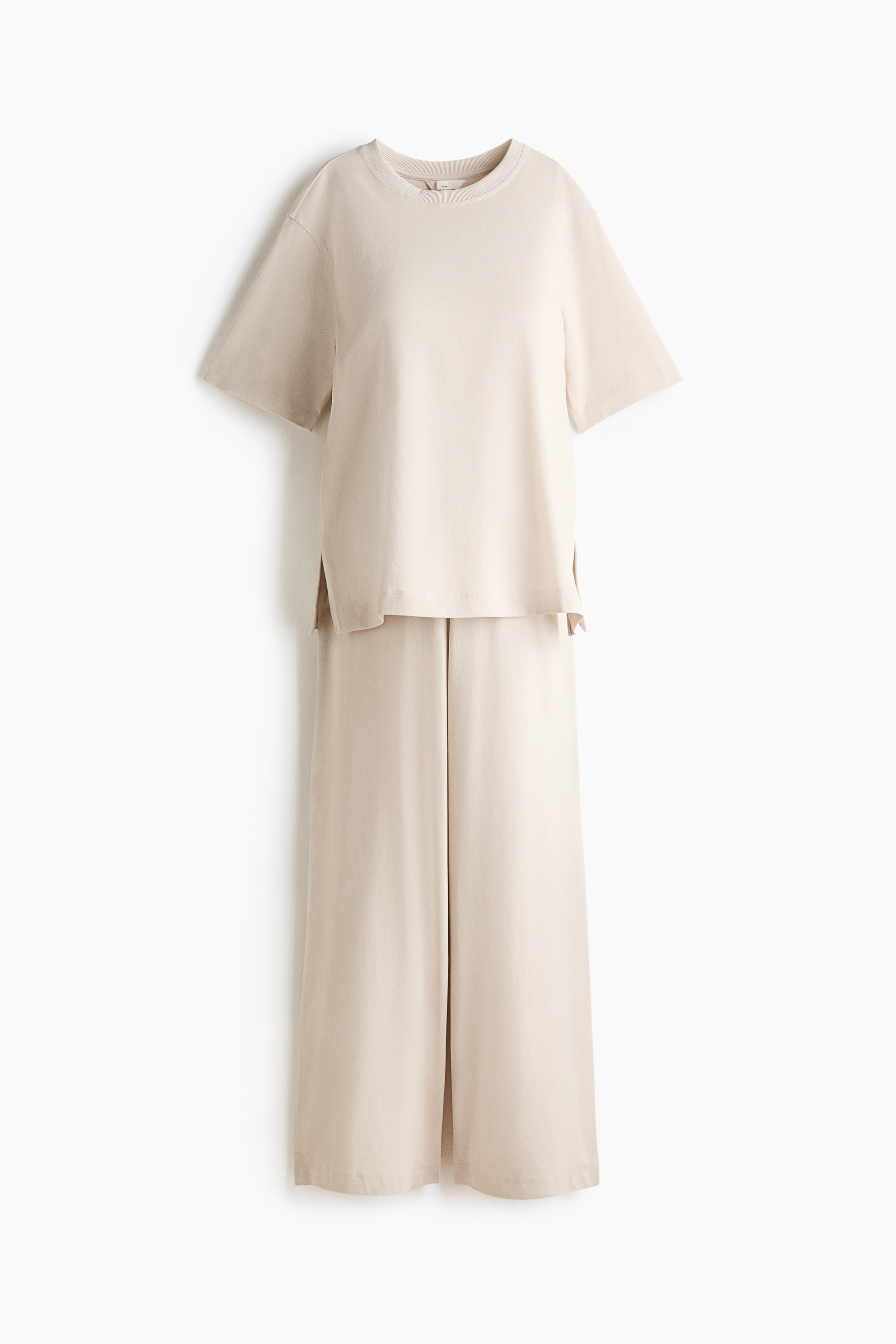 View larger image: A light beige two-piece loungewear set is shown from the front, featuring a short-sleeved T-shirt with a round neck and side slits, paired with wide-leg cropped trousers.