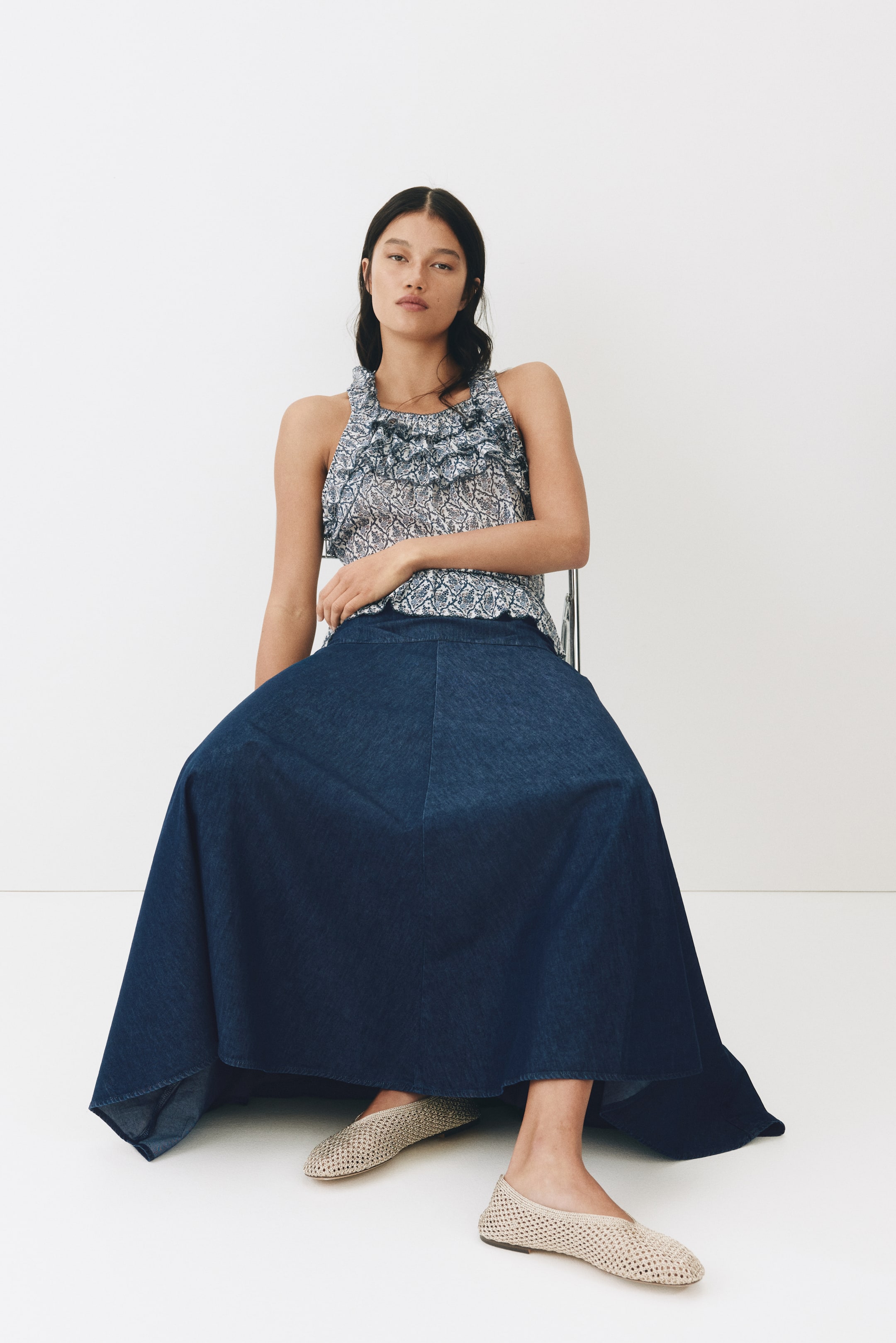 Agrandir l'image: Un haut sans manches, arborant un motif complexe bleu et blanc et un col à volants, est associé à une jupe longue en denim bleu foncé. La jupe ample s'évase à partir de la taille, révélant sa silhouette large alors qu'elle tombe élégamment.